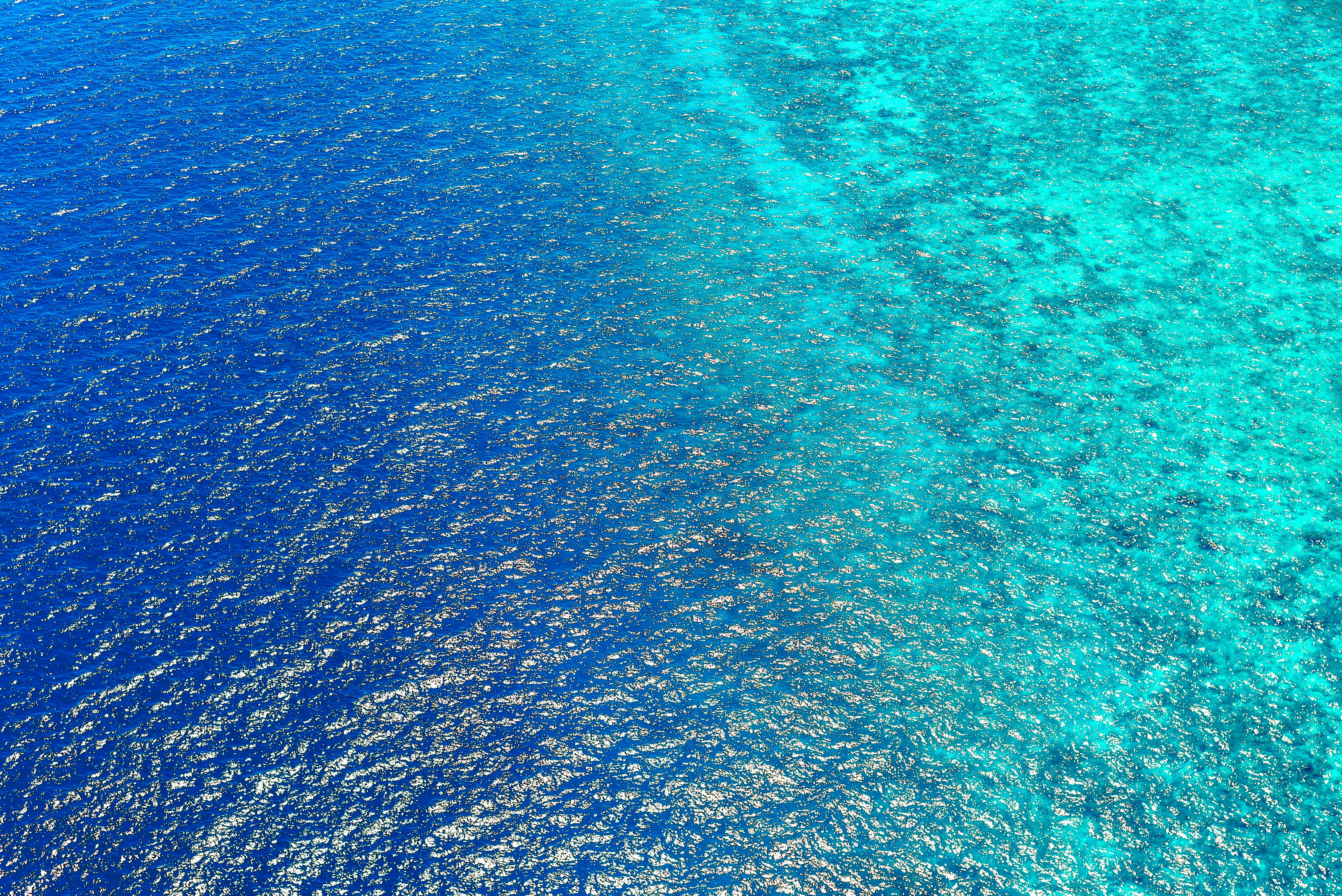 An aerial view of the ocean, half is deep blue, half is light green. - free wallpaper image