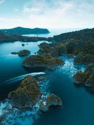 An aerial view of a turquoise sea surrounding rolling islands covered in lush green vegetation, with a light blue sky in the distance. The scene is tranquil and beautiful. - free wallpaper image