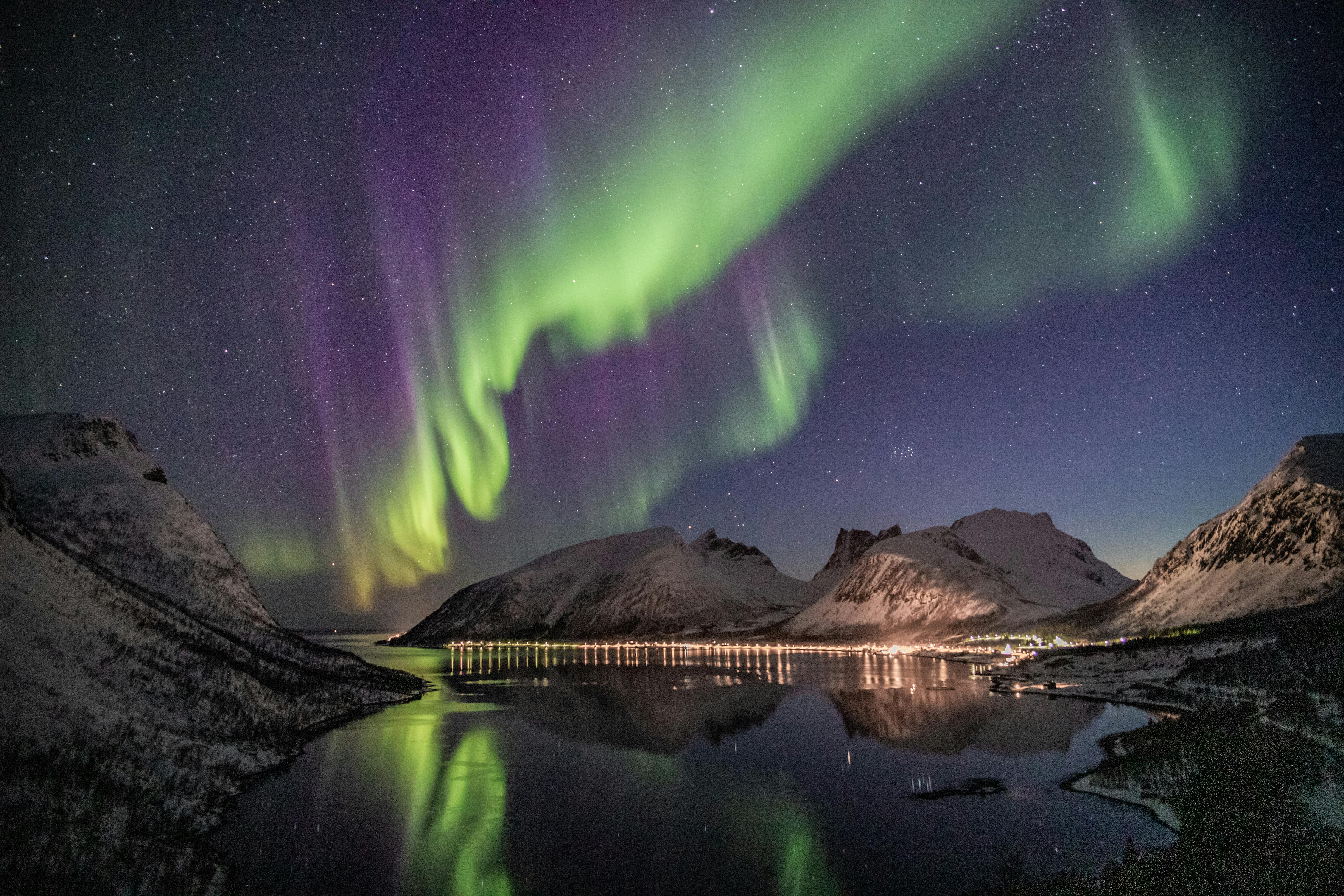 A beautiful aurora borealis shines in the night sky, reflecting on the calm lake, with mountains in the distance. - free wallpaper image