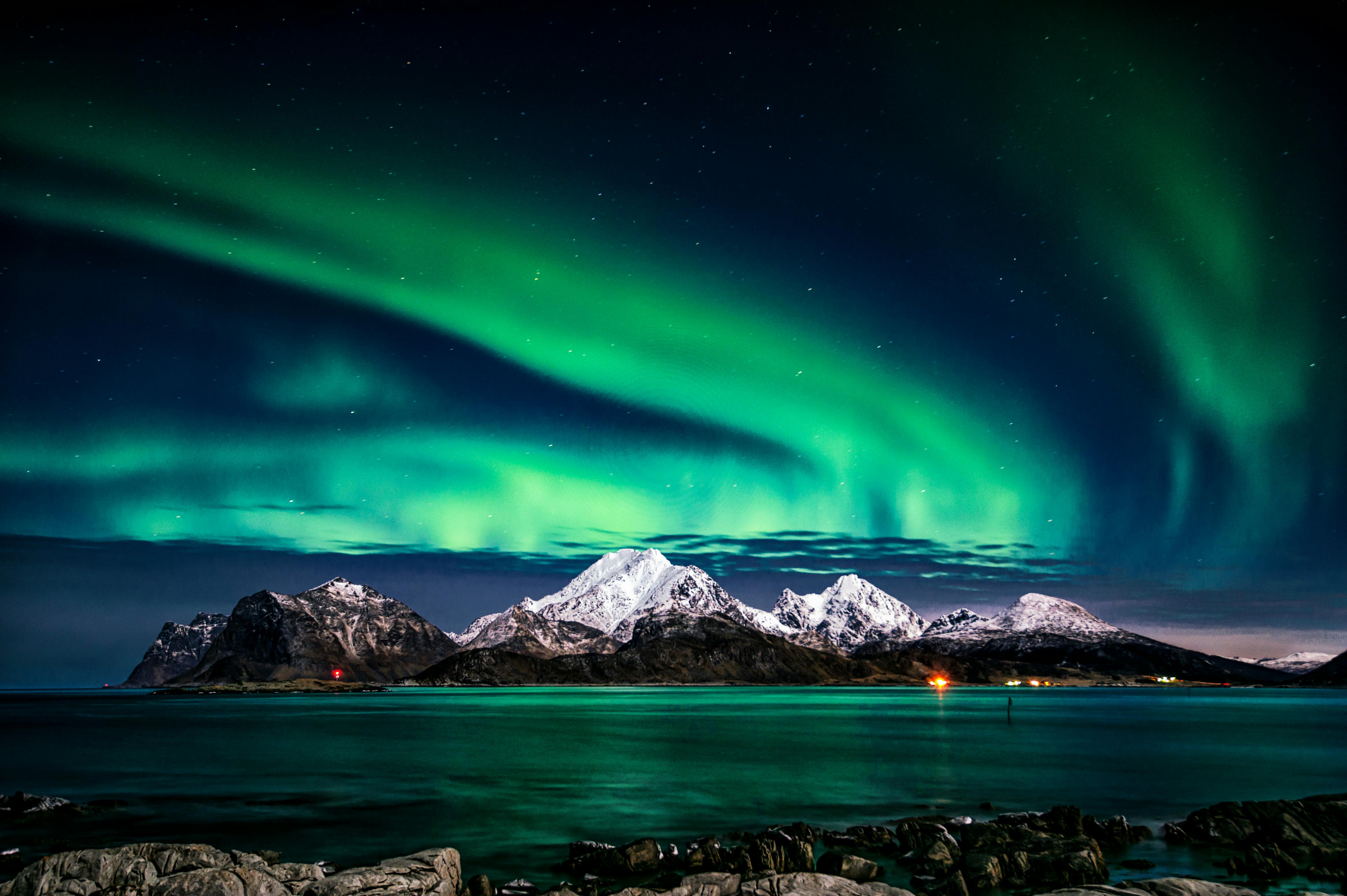 A stunning green aurora borealis fills the night sky, set against a backdrop of snow-capped mountains and a calm sea. - free wallpaper image