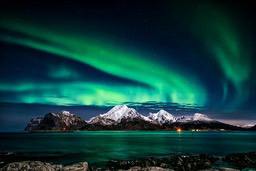 A stunning green aurora borealis fills the night sky, set against a backdrop of snow-capped mountains and a calm sea. - free wallpaper image