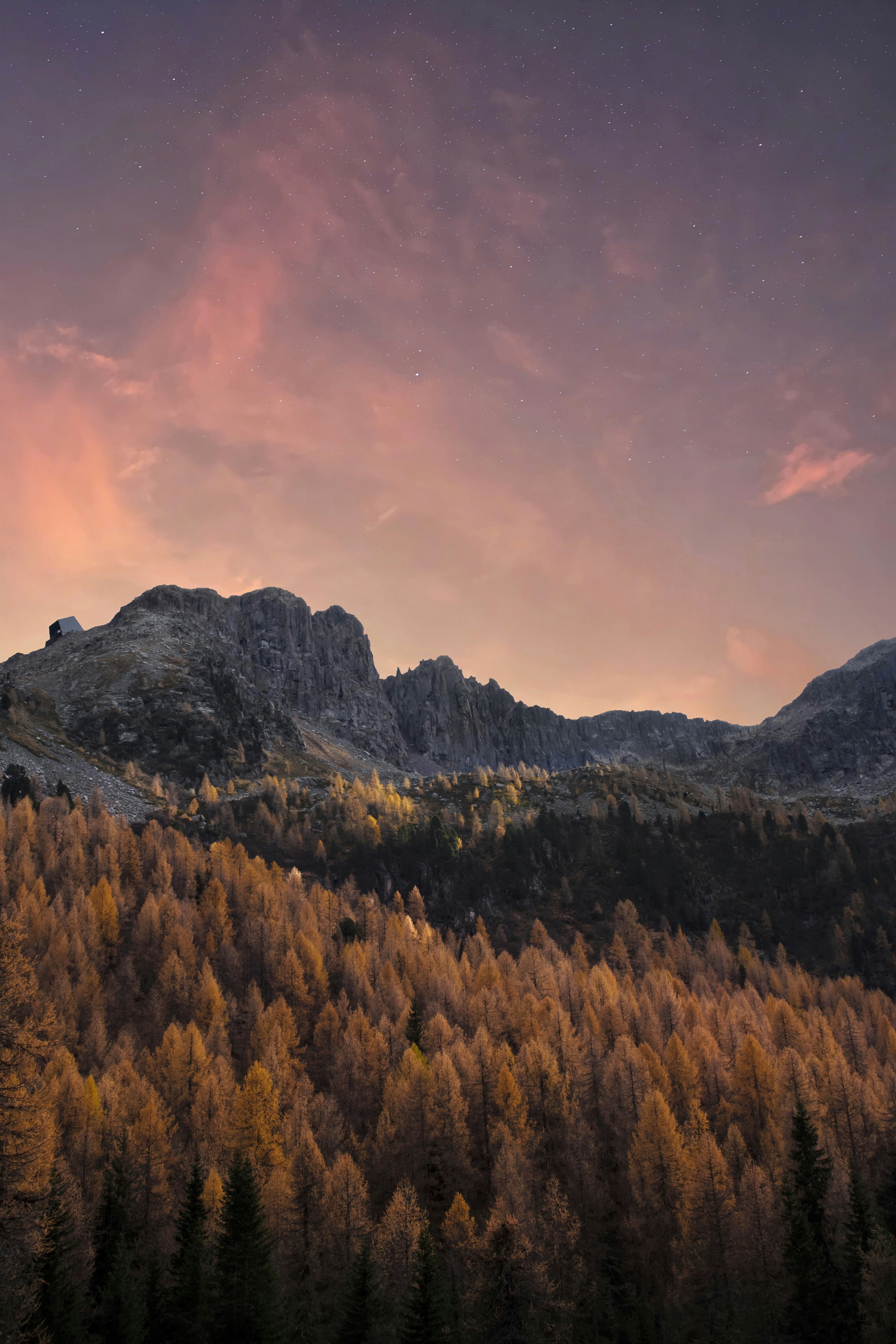 The sky is a vibrant purple and orange as the sun sets, casting a golden glow on the autumnal trees in the mountains. - free wallpaper image