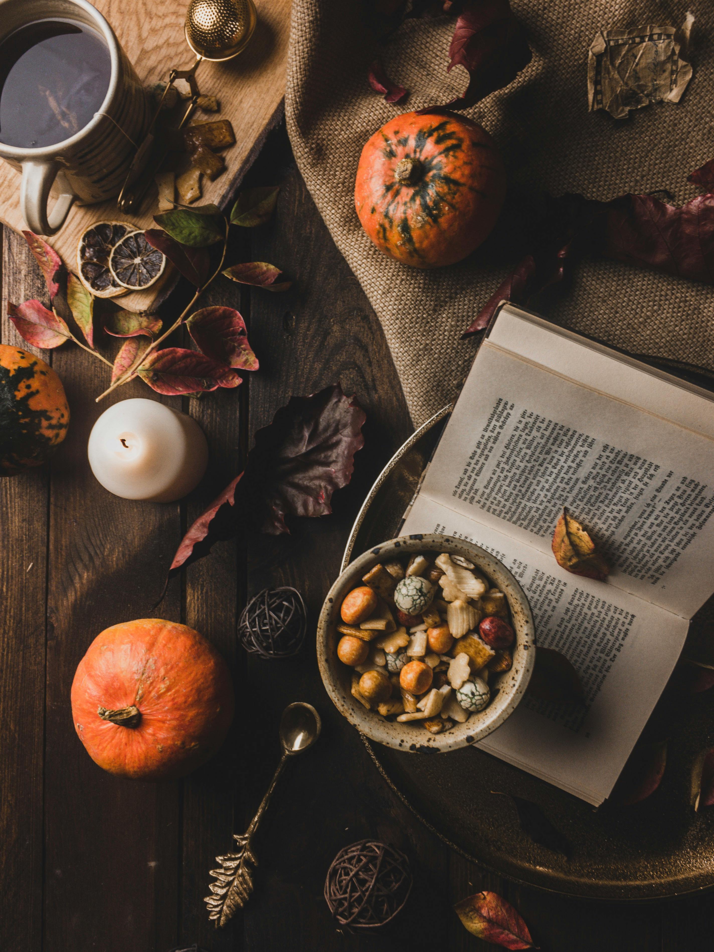 A wooden table with pumpkins, dry flowers, a teacup, a book and a bowl of snacks, creating a warm and comfortable autumn atmosphere. - wallpaper image