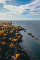 A road winds along the coastline, lined with trees in autumn colors, the sea in the distance is calm and vast. - free wallpaper image