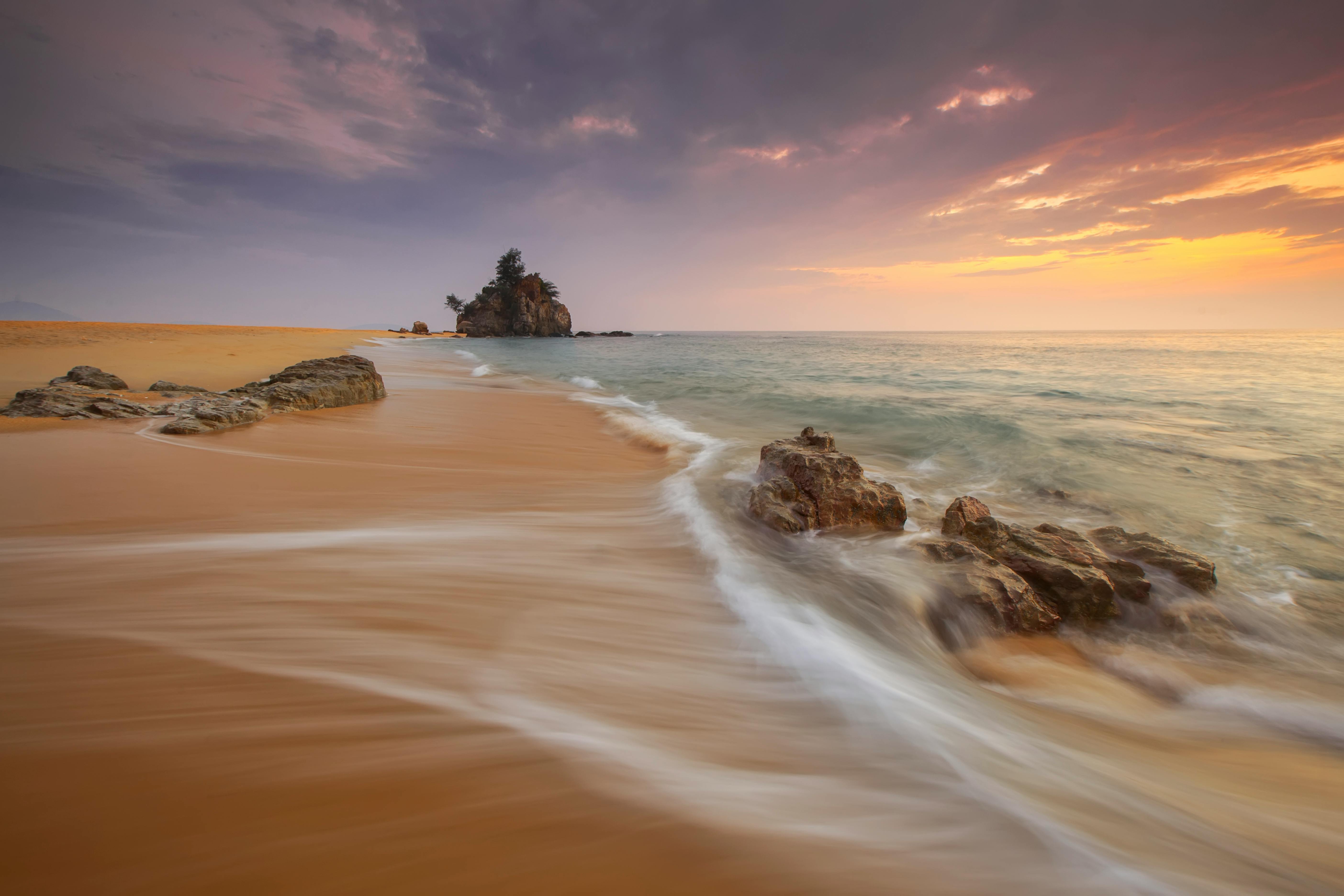 The waves crash against the rocks on the beach, the sea in the distance is bathed in a golden glow, and the sky is a beautiful sunset. - free wallpaper image