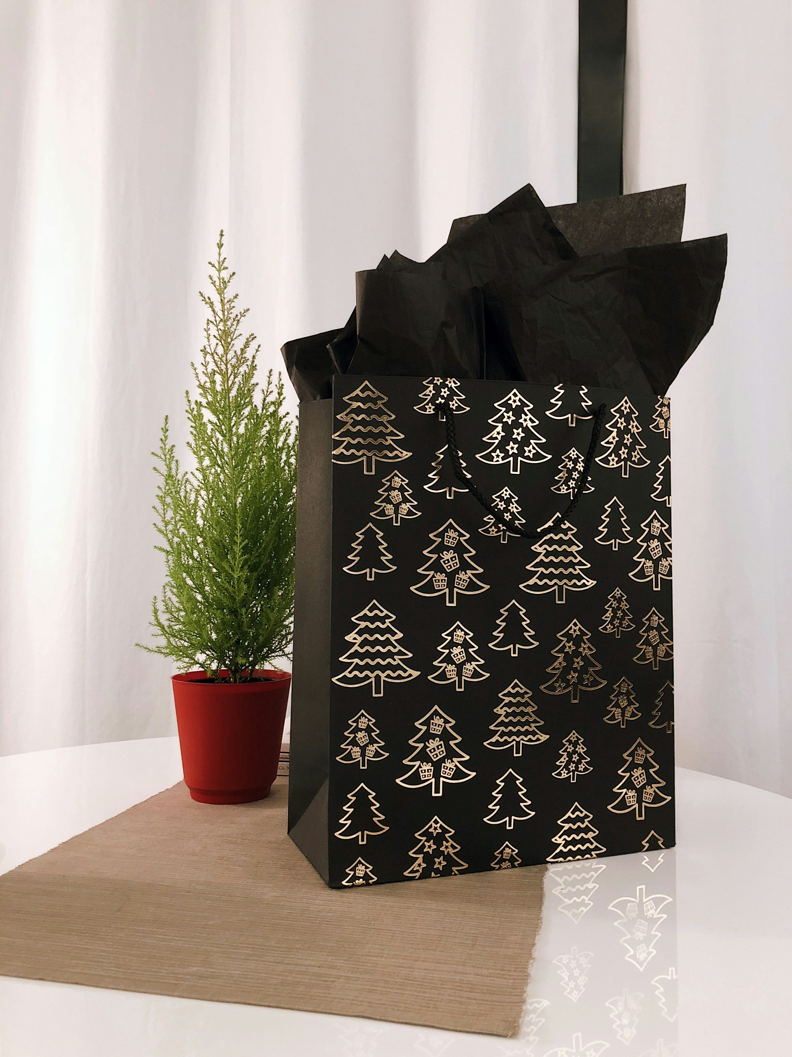 A black Christmas gift bag is placed on the table, with golden Christmas trees printed on it, and a black piece of paper inside. - wallpaper image