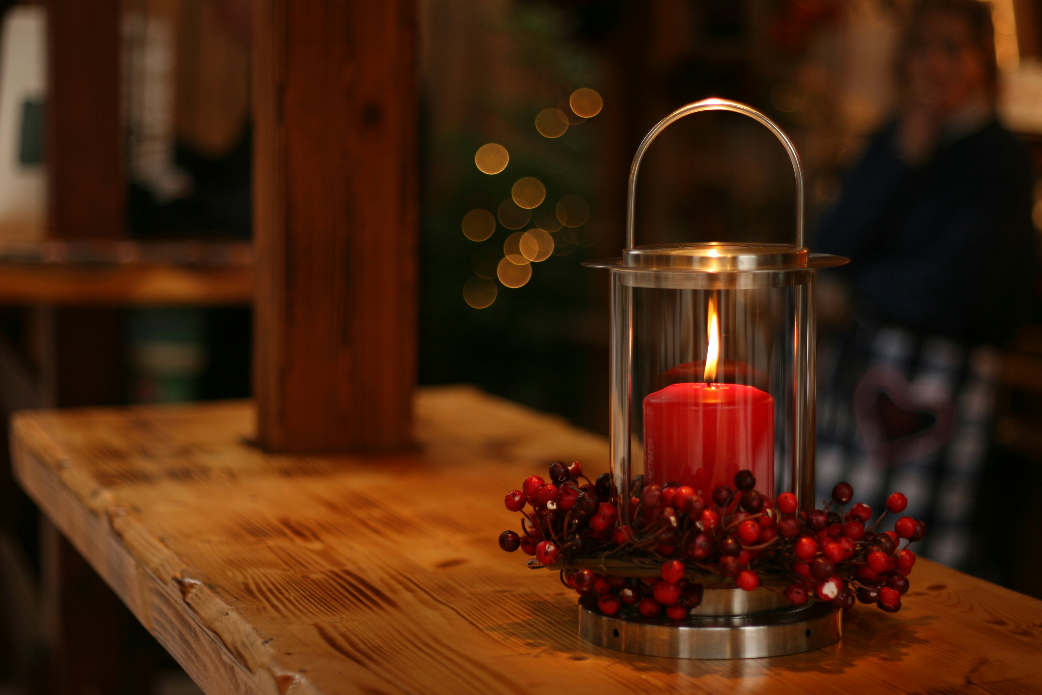 A silver candle holder with a red candle burning on a wooden table. - wallpaper image