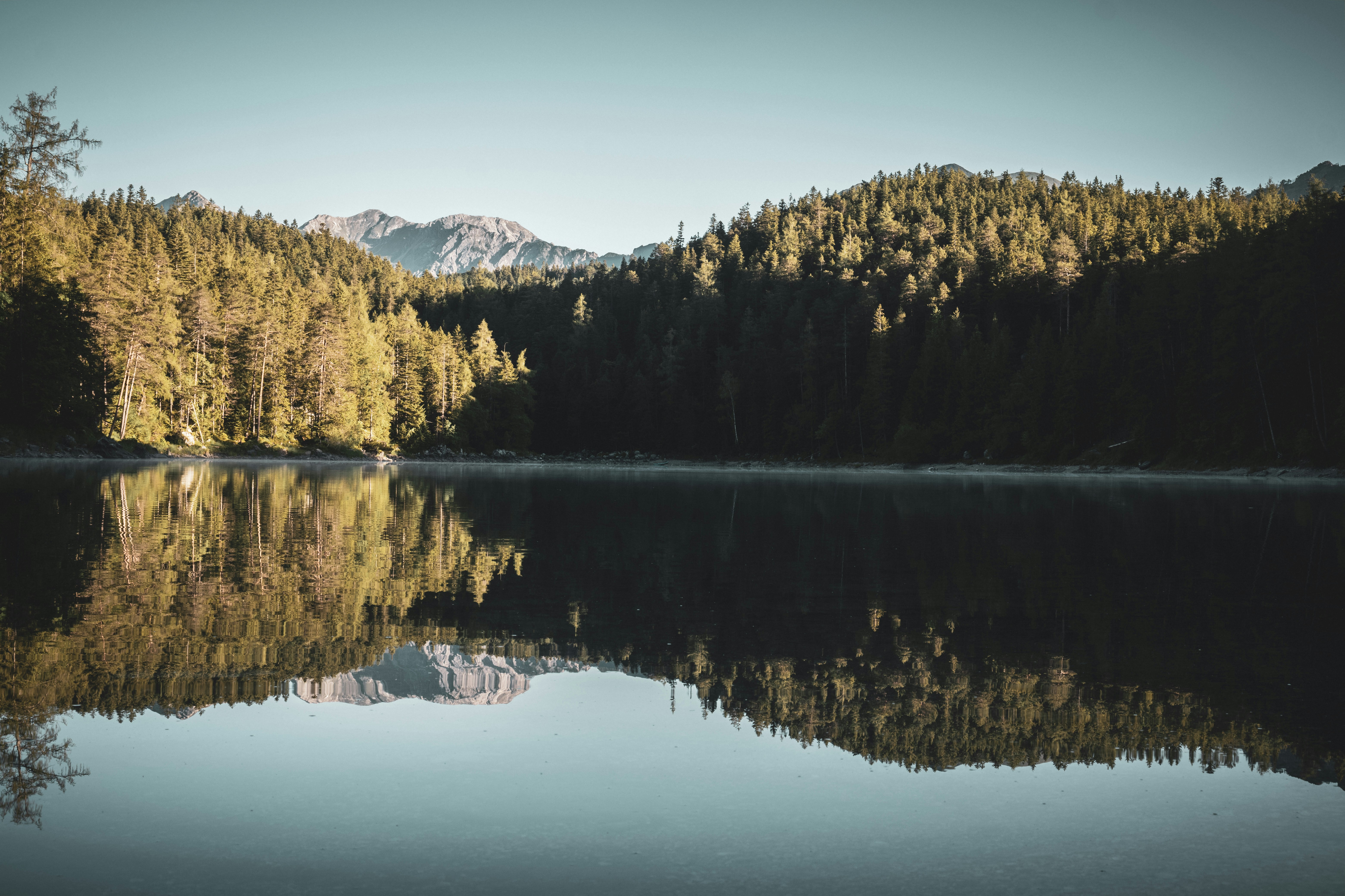 A calm lake reflecting the mountains and forests, the sky is blue and the scenery is peaceful and beautiful. - free wallpaper image