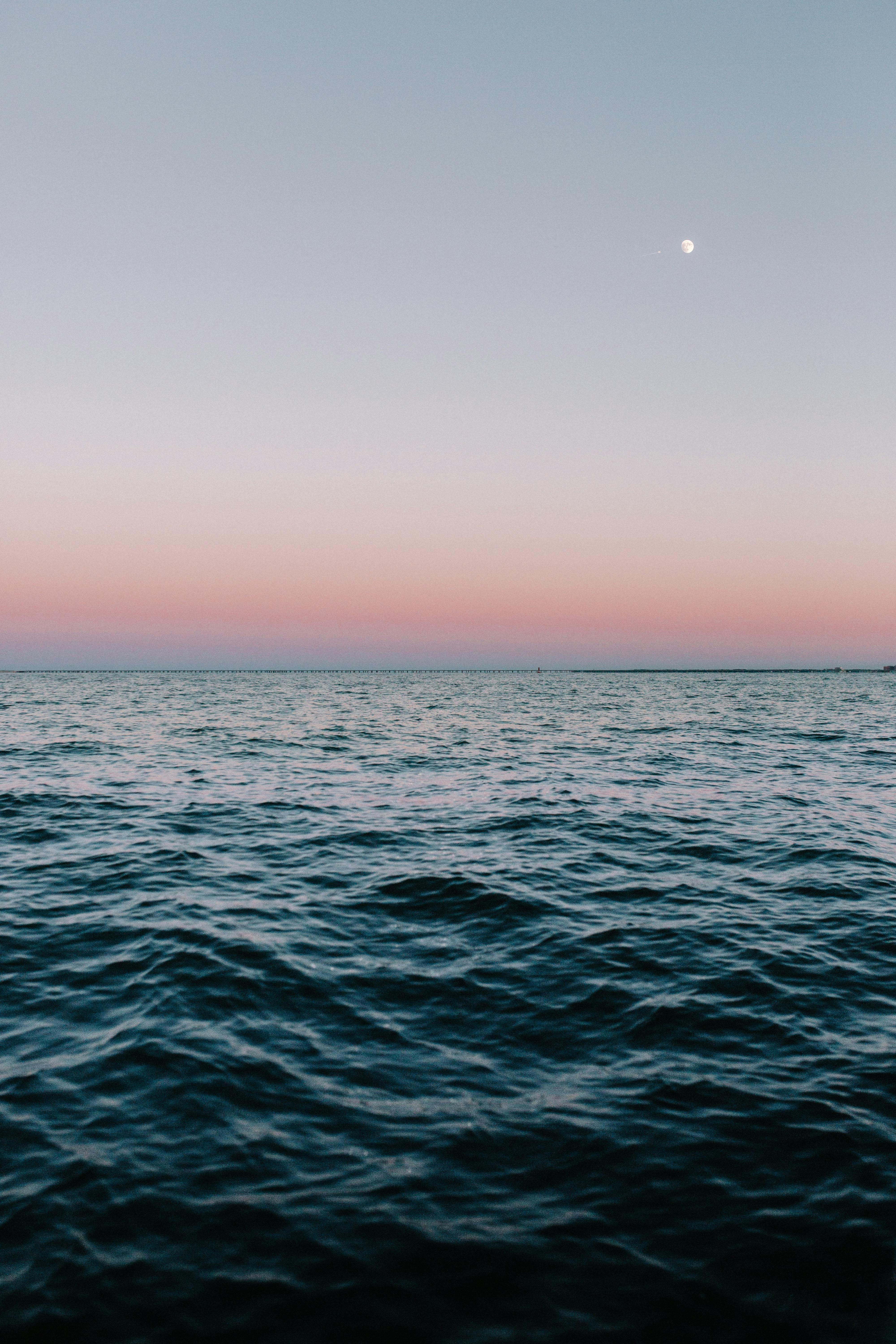 The calm sea surface is rippling, there is a crescent moon in the night sky in the distance, and the horizon is tinged with a faint pink, heralding the arrival of dawn. - free wallpaper image