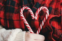 Two candy canes are held in hand, forming a heart shape against a red and black plaid cloth. - wallpaper image