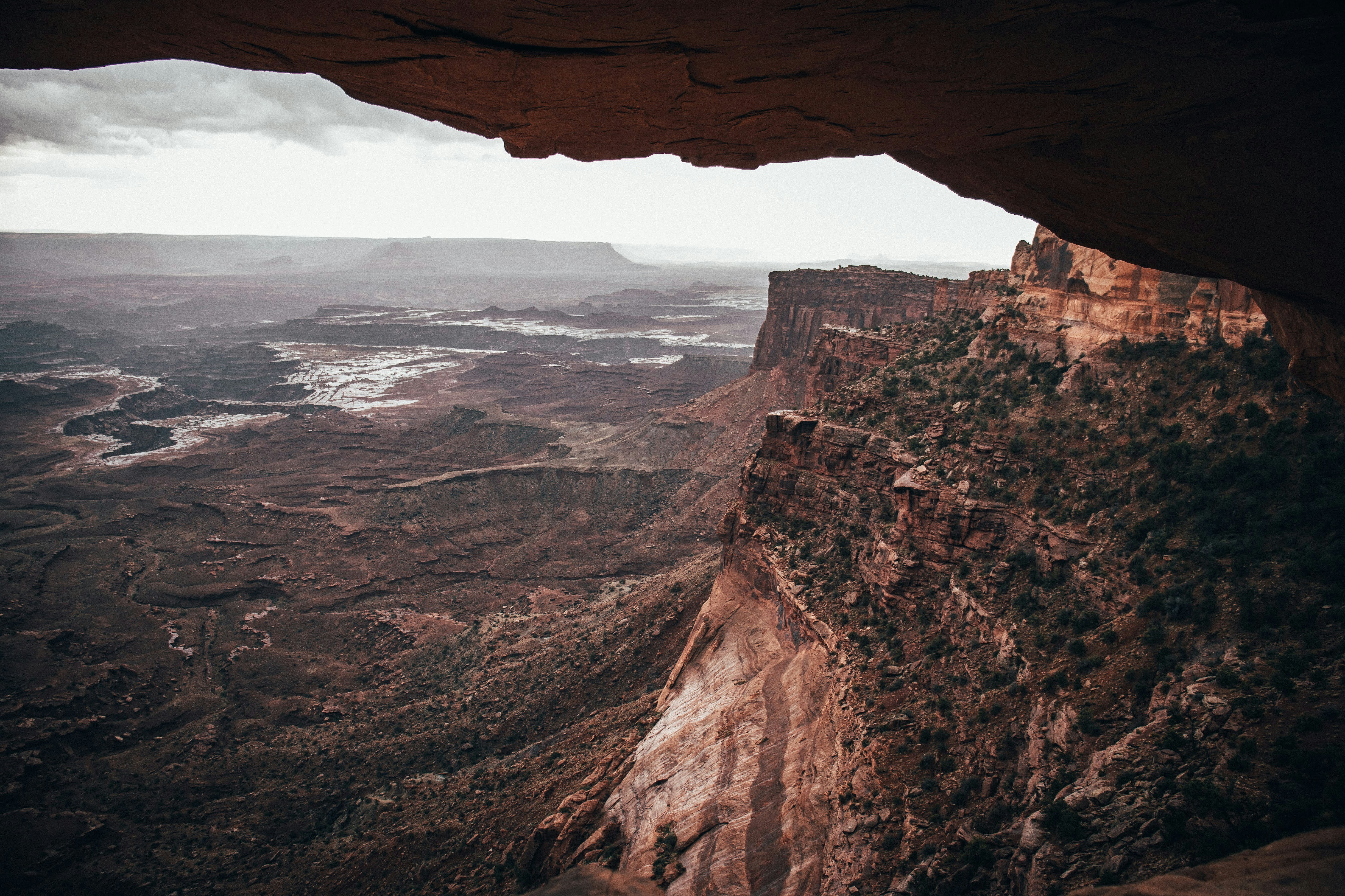 A vast canyon landscape with layered mountains and rocks viewed from a rock arch. - free wallpaper image