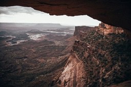 A vast canyon landscape with layered mountains and rocks viewed from a rock arch. - free wallpaper image