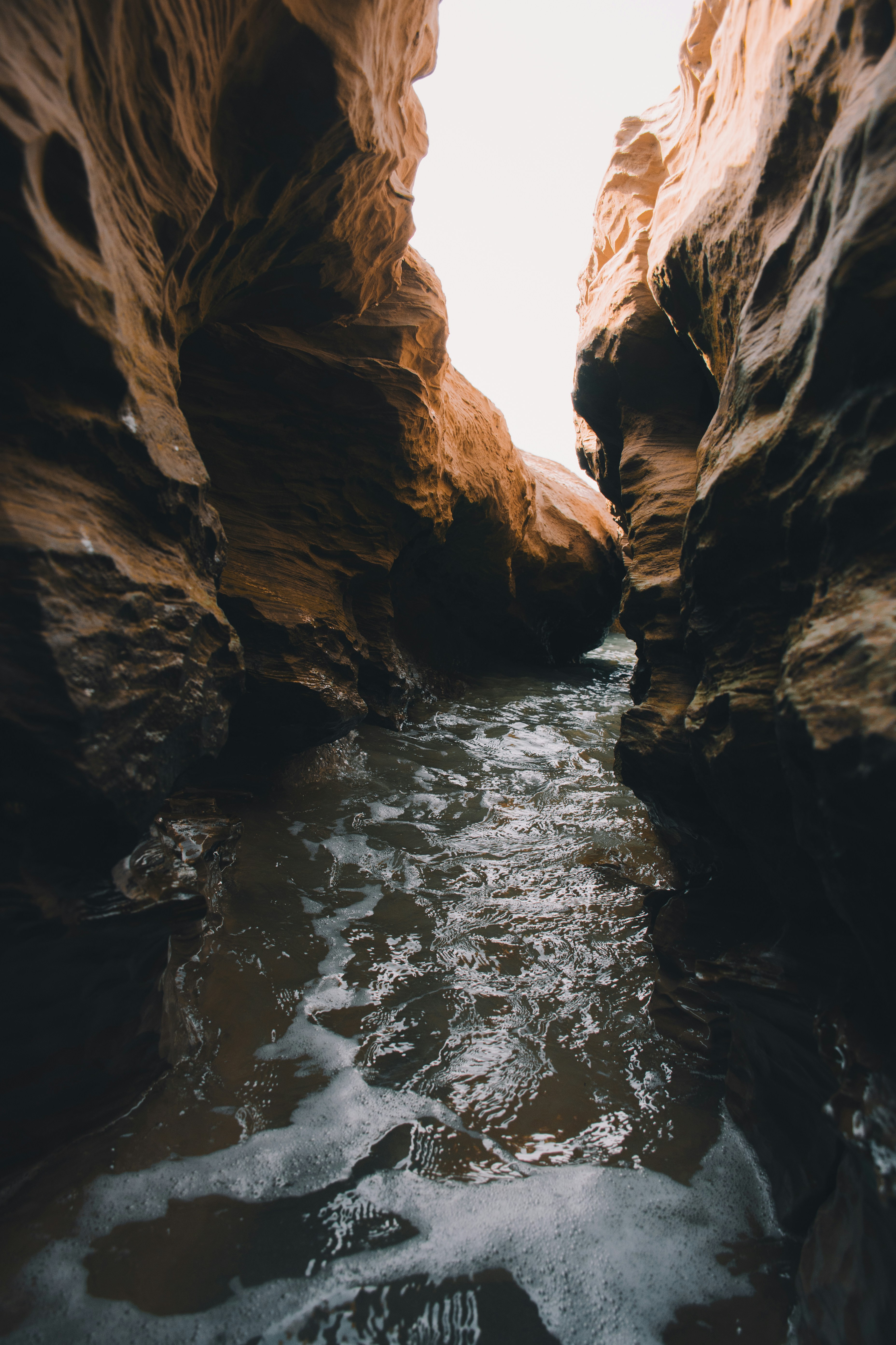 A stream flows through a narrow canyon, with towering rock cliffs on either side. - free wallpaper image