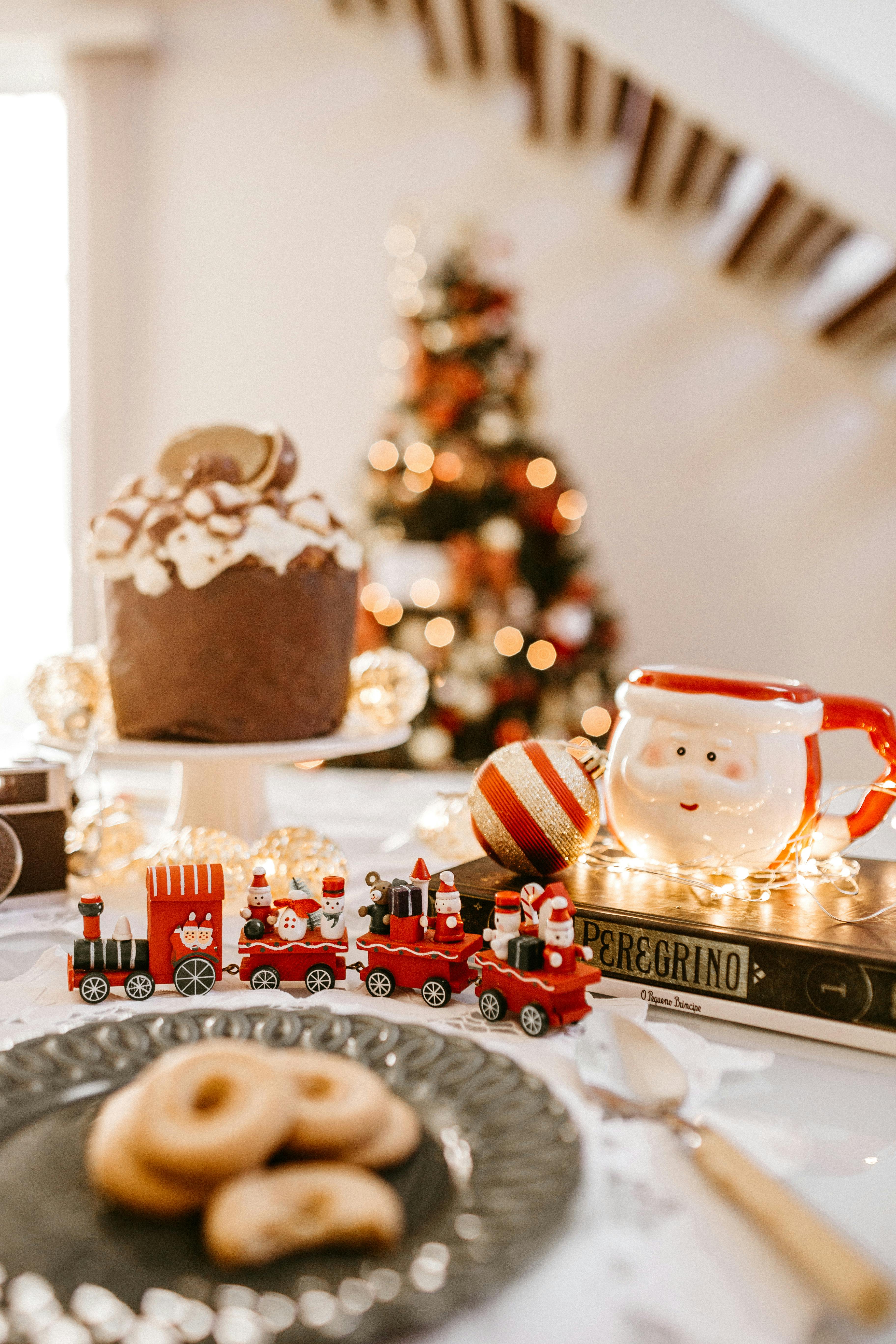 A Christmas table setting with a Christmas cake, a Santa Claus mug, a toy train decoration and some other snacks. - wallpaper image