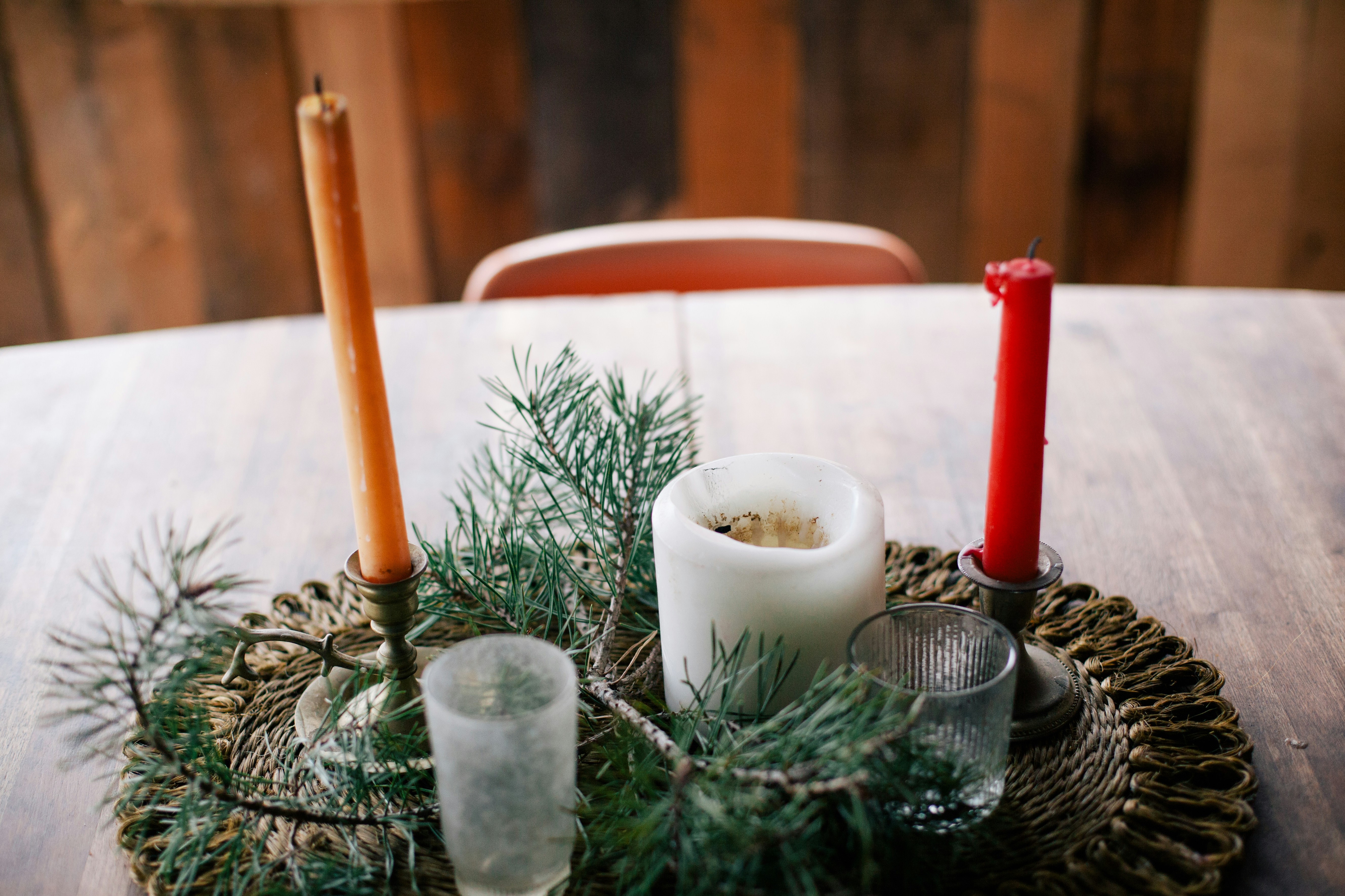 Two candlesticks and a white candle are placed on a wooden table, with two glasses and some green pine branches next to them. - wallpaper image