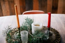 Two candlesticks and a white candle are placed on a wooden table, with two glasses and some green pine branches next to them. - wallpaper image