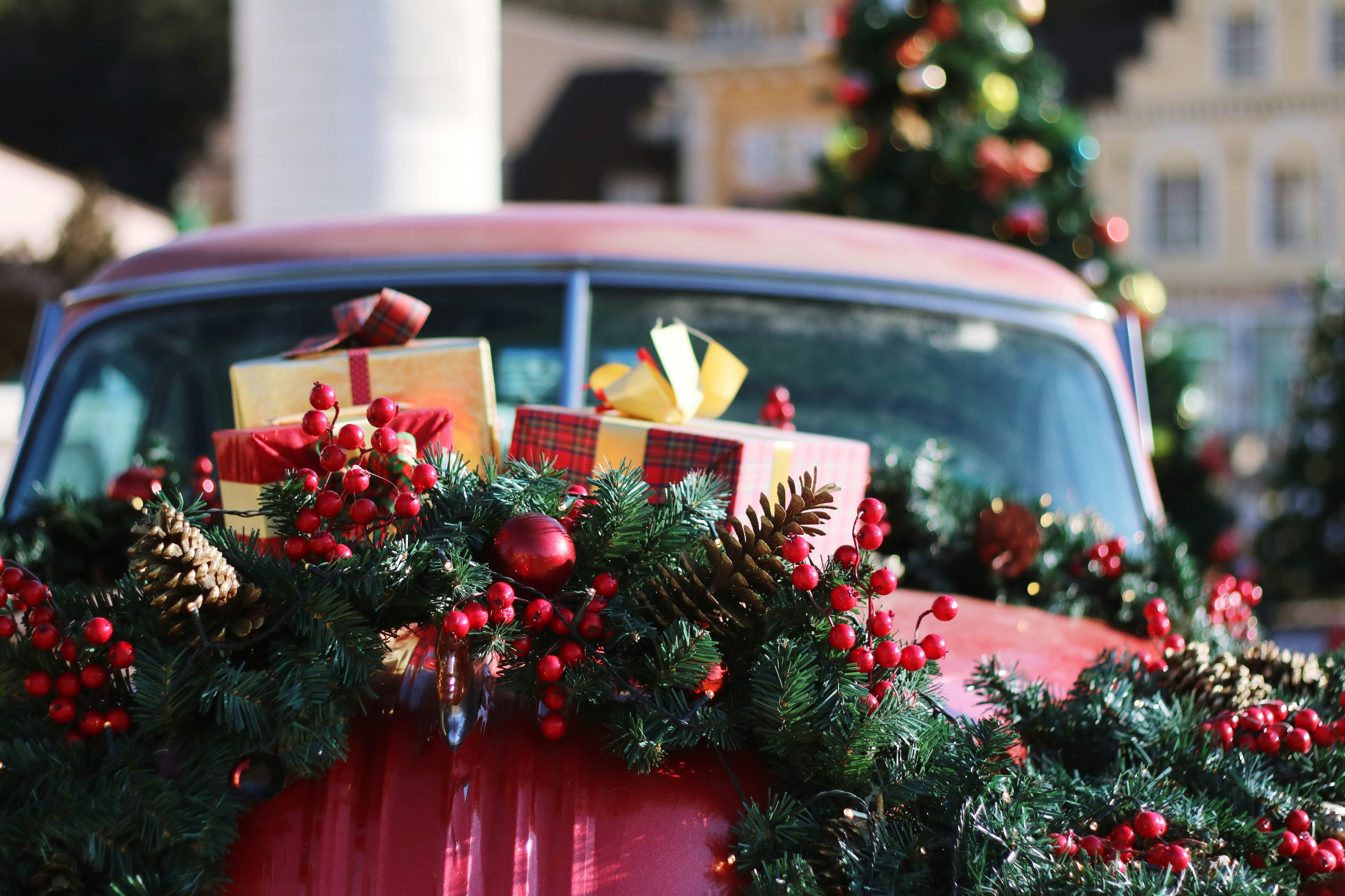 A red car is decorated with Christmas tree branches, red berries, golden pine cones and gifts, creating a strong Christmas atmosphere. - wallpaper image