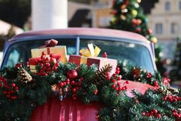 A red car is decorated with Christmas tree branches, red berries, golden pine cones and gifts, creating a strong Christmas atmosphere. - wallpaper image