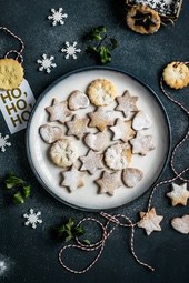 A white plate with many Christmas cookies decorated with powdered sugar, surrounded by red and white ropes, snowflake decorations and green leaves. - wallpaper image