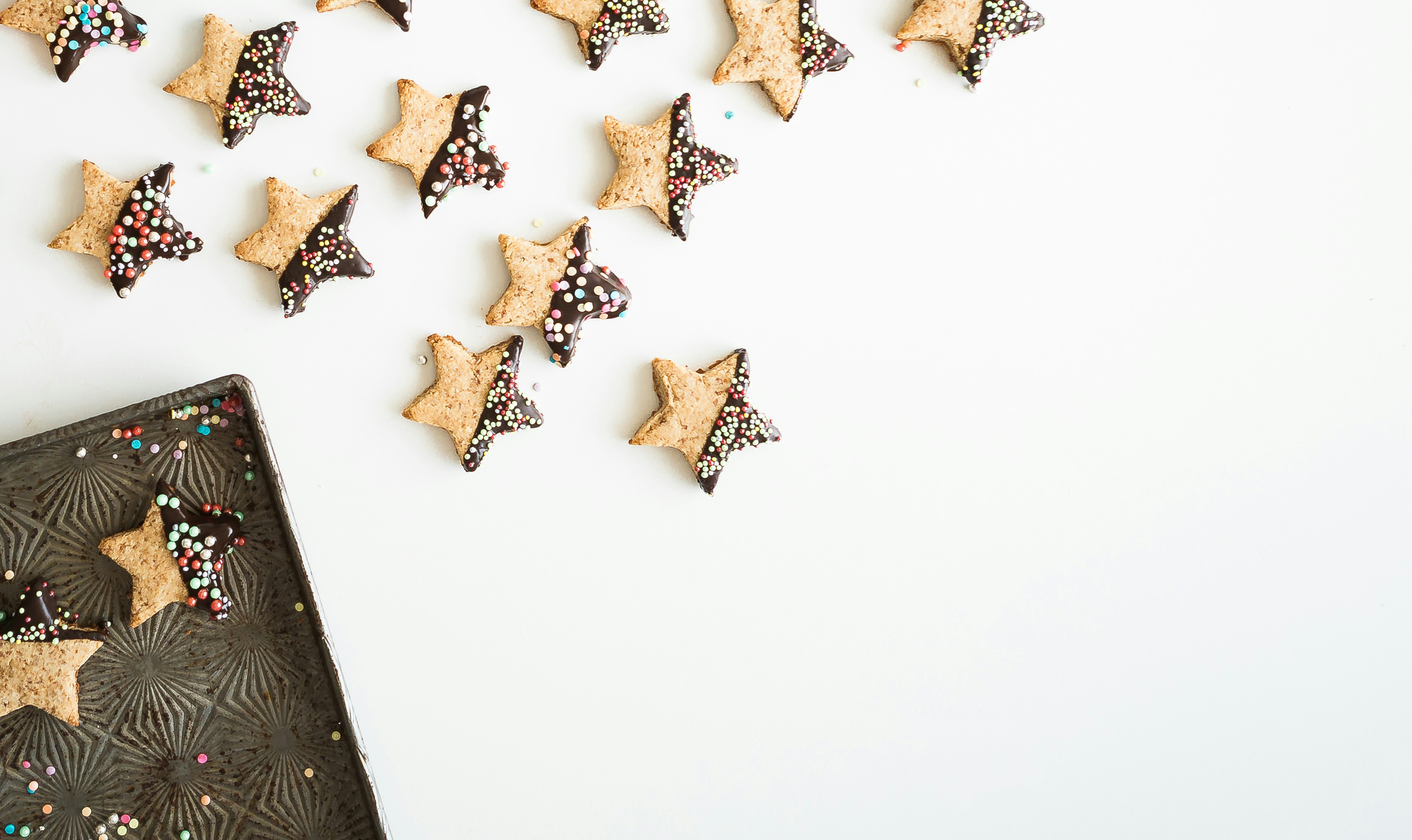 Star-shaped cookies with chocolate sauce and colorful sprinkles on a white background. - wallpaper image