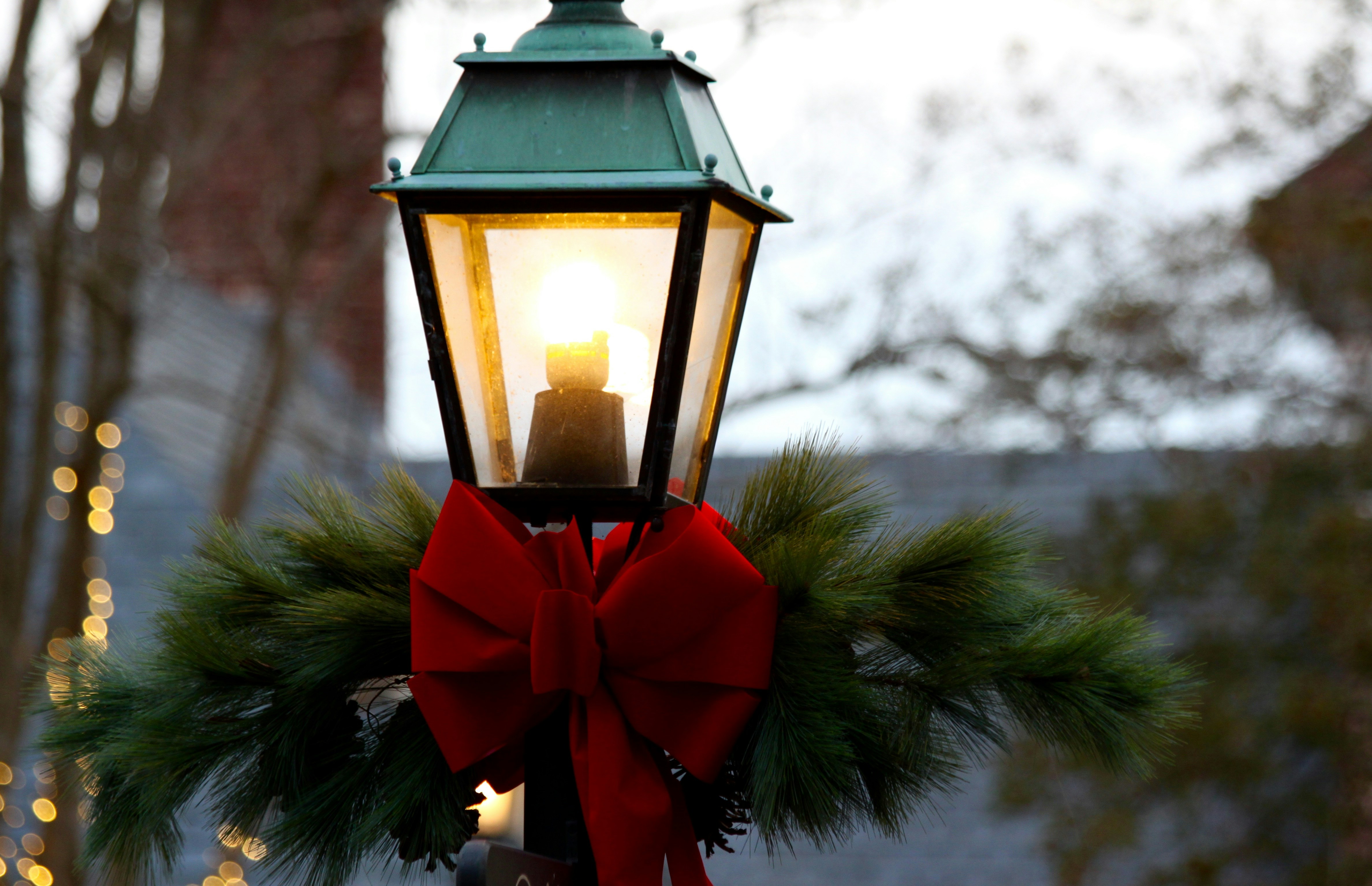 A street lamp decorated with Christmas tree branches and a red ribbon. The light bulb is on, emitting a warm glow. - wallpaper image