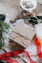 A wrapped gift box on a white tablecloth, surrounded by Christmas decorations like green branches, red ribbons and a glass jar filled with cookies. - wallpaper image