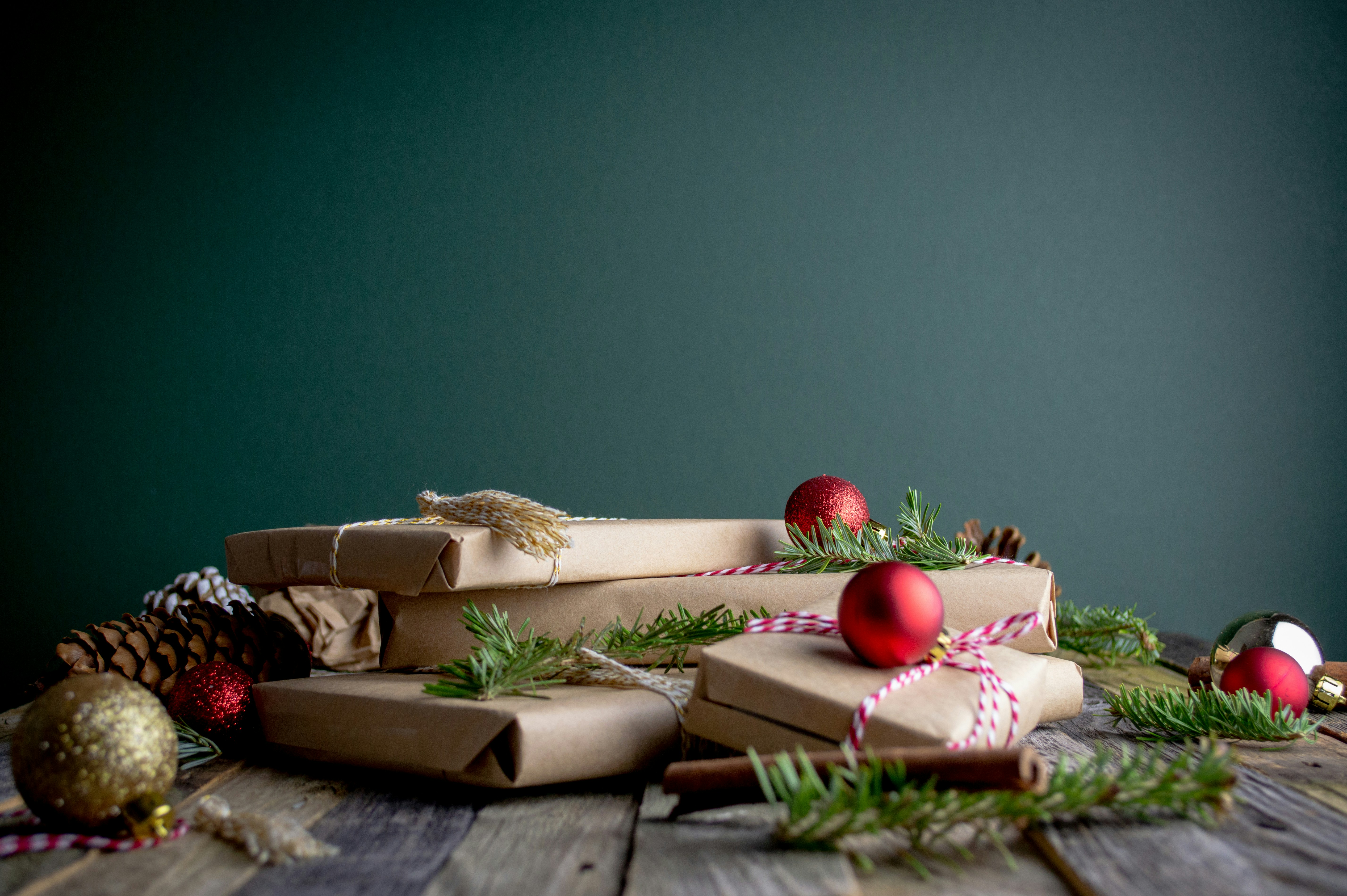 Some gift boxes wrapped in brown paper are placed on a wooden table, decorated with Christmas branches, pine cones and red Christmas balls. - wallpaper image