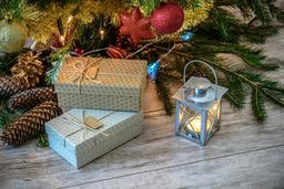 Underneath the Christmas tree, there are two presents, a silver lantern with a warm light on, beside pine cones and branches. - wallpaper image