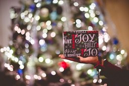 A hand holding a Christmas present, the background is a blurred Christmas tree lights. - wallpaper image