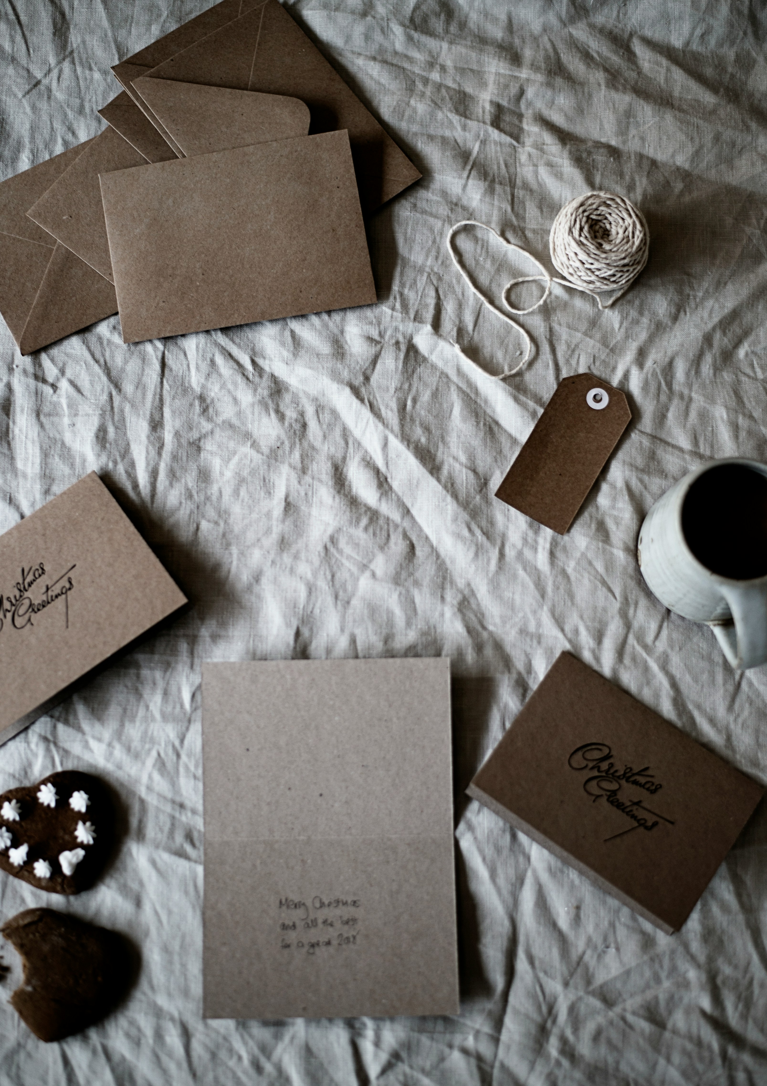 Some envelopes, cards, candies, yarn and a ceramic cup are placed on a white cloth, the overall color tone is warm and simple, creating a warm and comfortable atmosphere. - wallpaper image