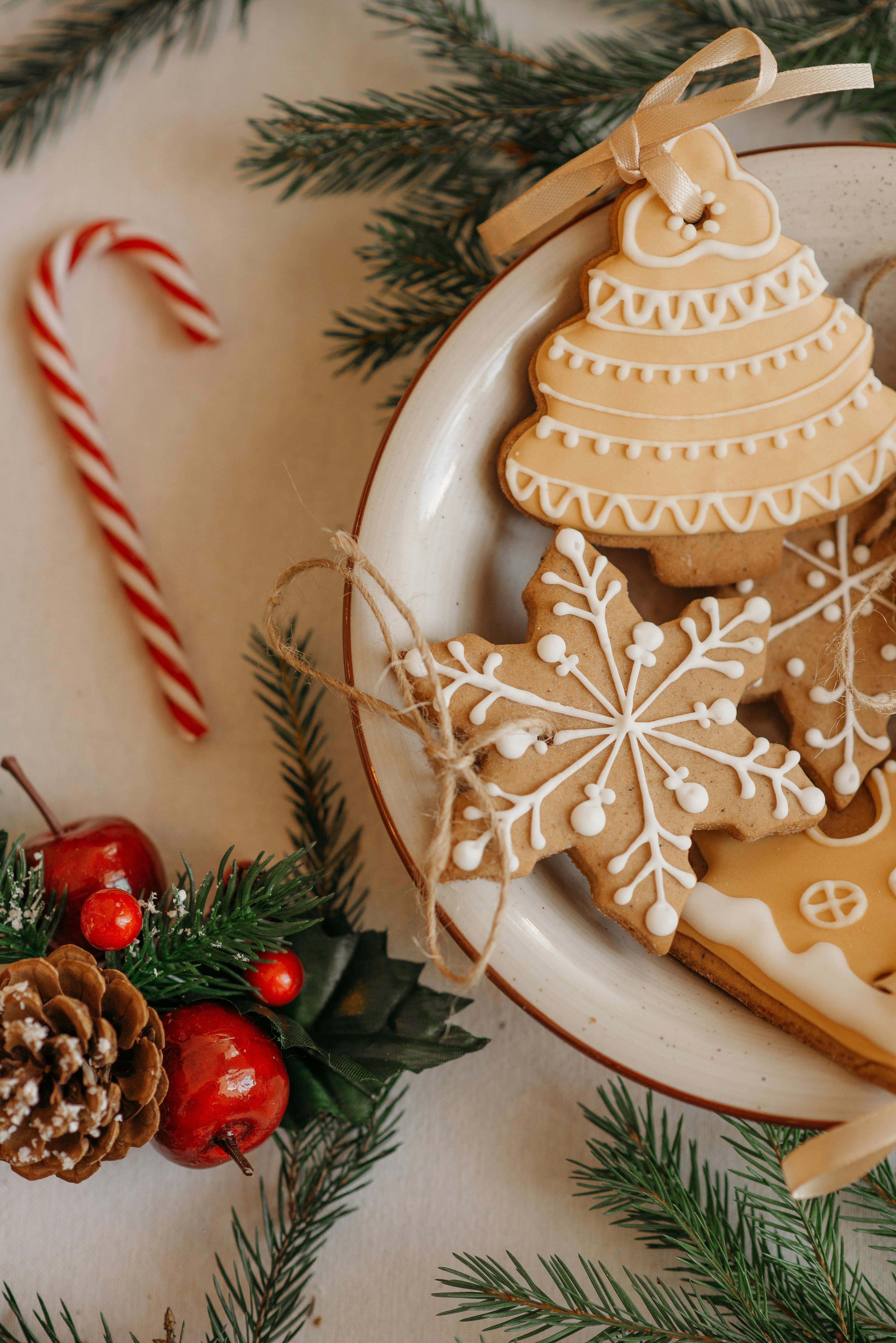 On a white background, a white plate contains some gingerbread cookies, including a gingerbread tree, a gingerbread snowflake and a gingerbread house, decorated with Christmas tree branches and red berries. - wallpaper image