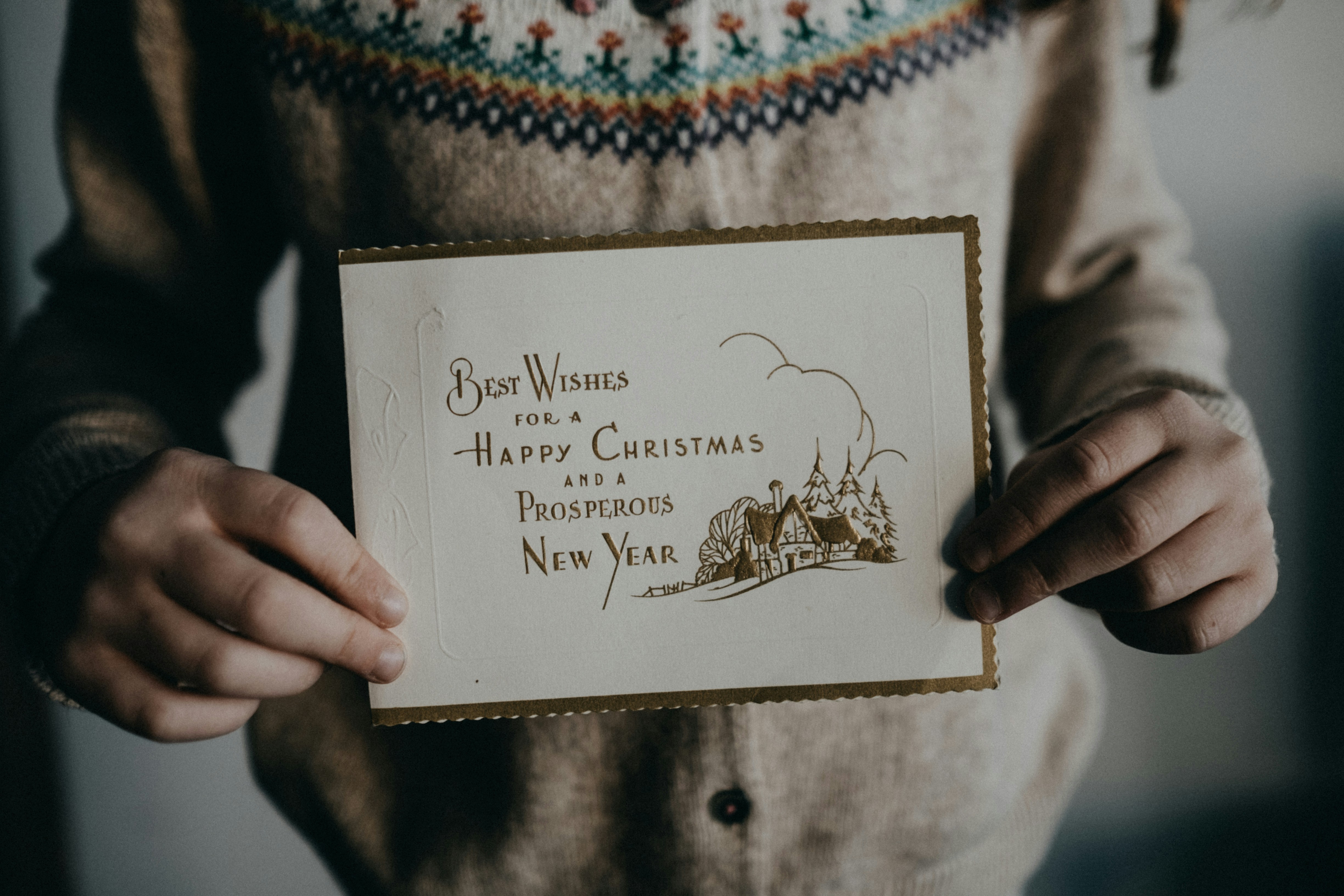 A young girl in a sweater is holding a Christmas card that says 'Best wishes for a Happy Christmas and a Prosperous New Year'. - wallpaper image