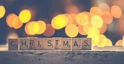 The word "CHRISTMAS" is spelled out with wooden letter tiles on a wooden surface with warm lights in the background - wallpaper image