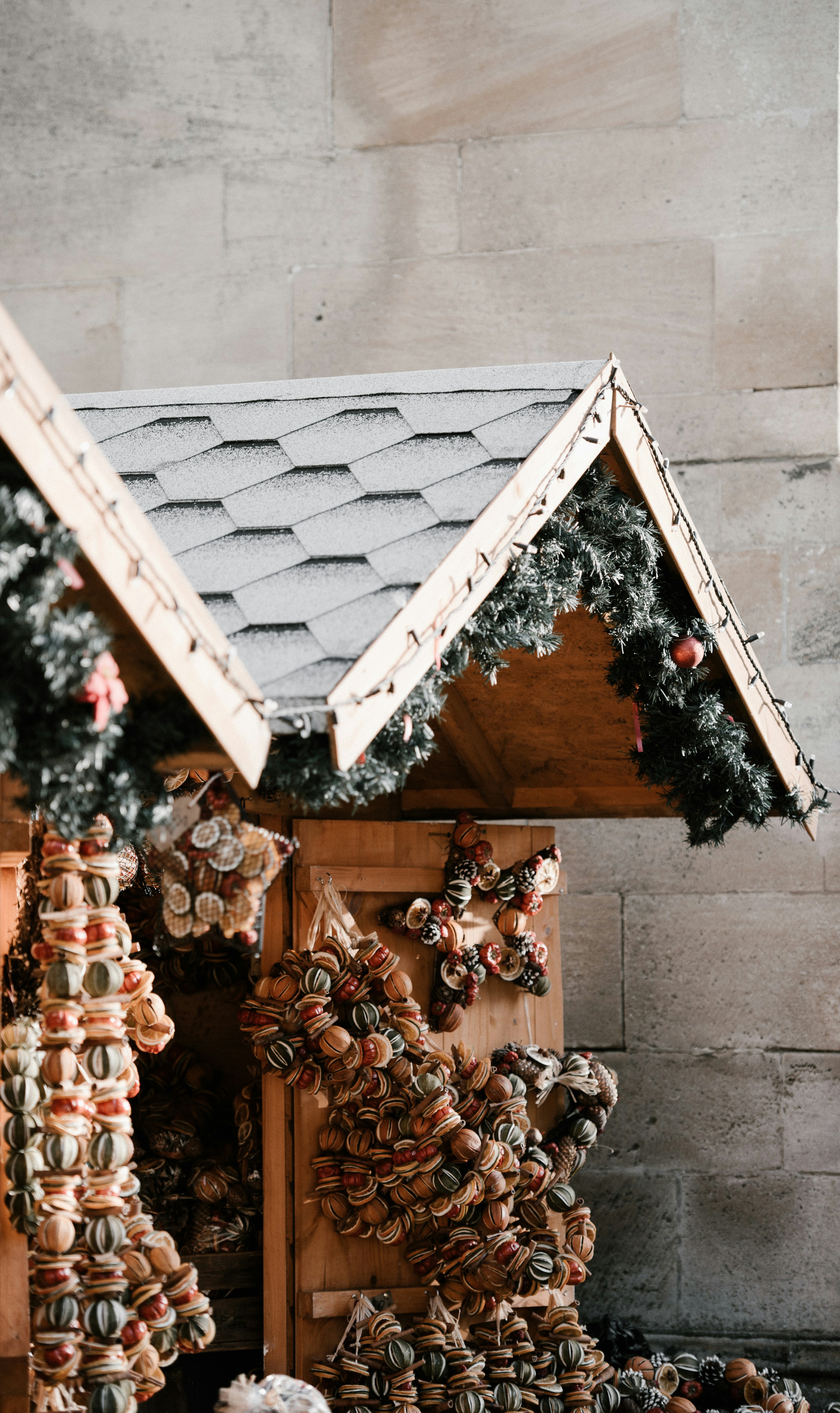 A wooden stall at a Christmas market decorated with dried fruits and pine cones, with a snowy roof and decorated with Christmas tree branches and fairy lights. - wallpaper image