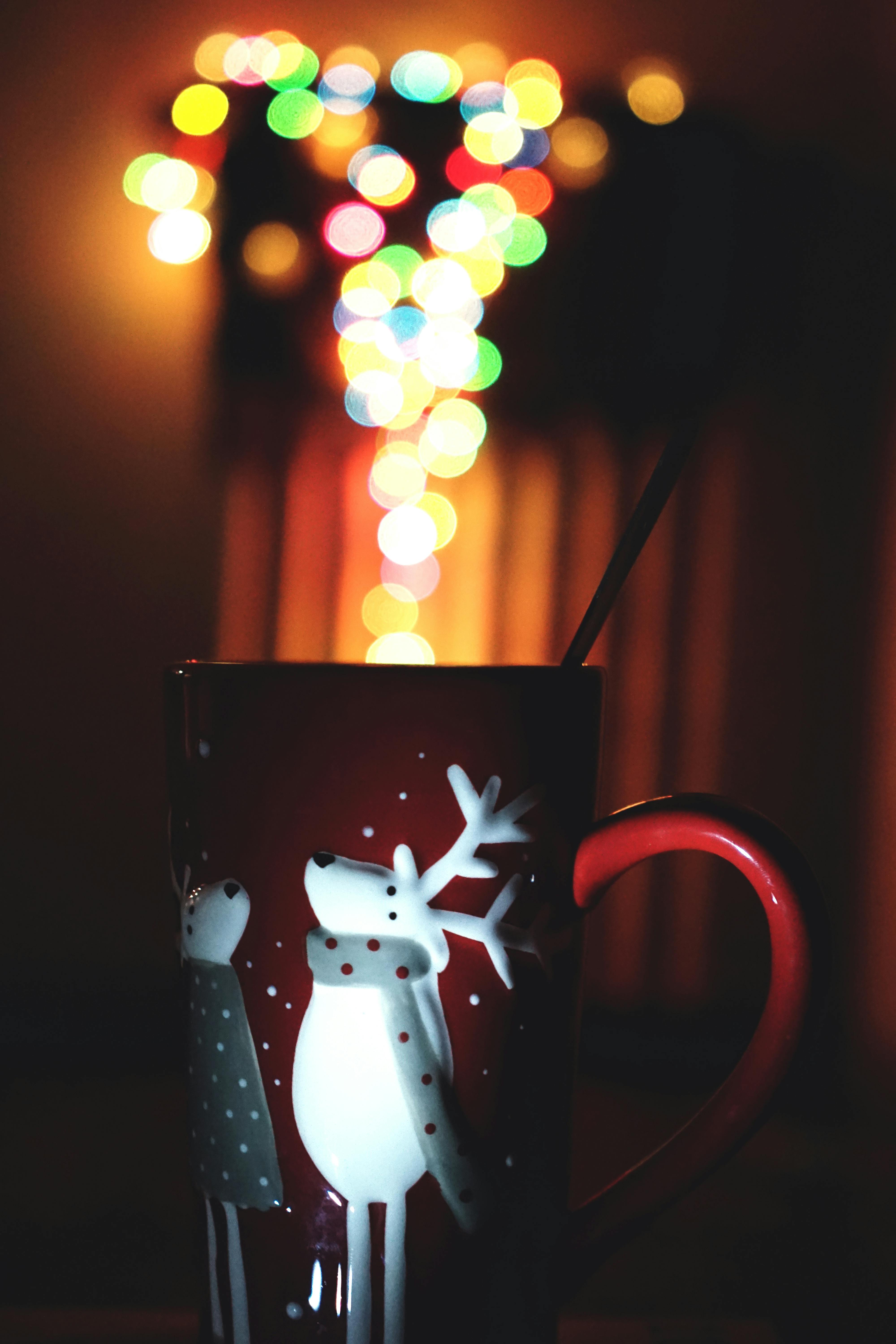 A red mug with a Christmas design, blurred colorful lights in the background. - wallpaper image