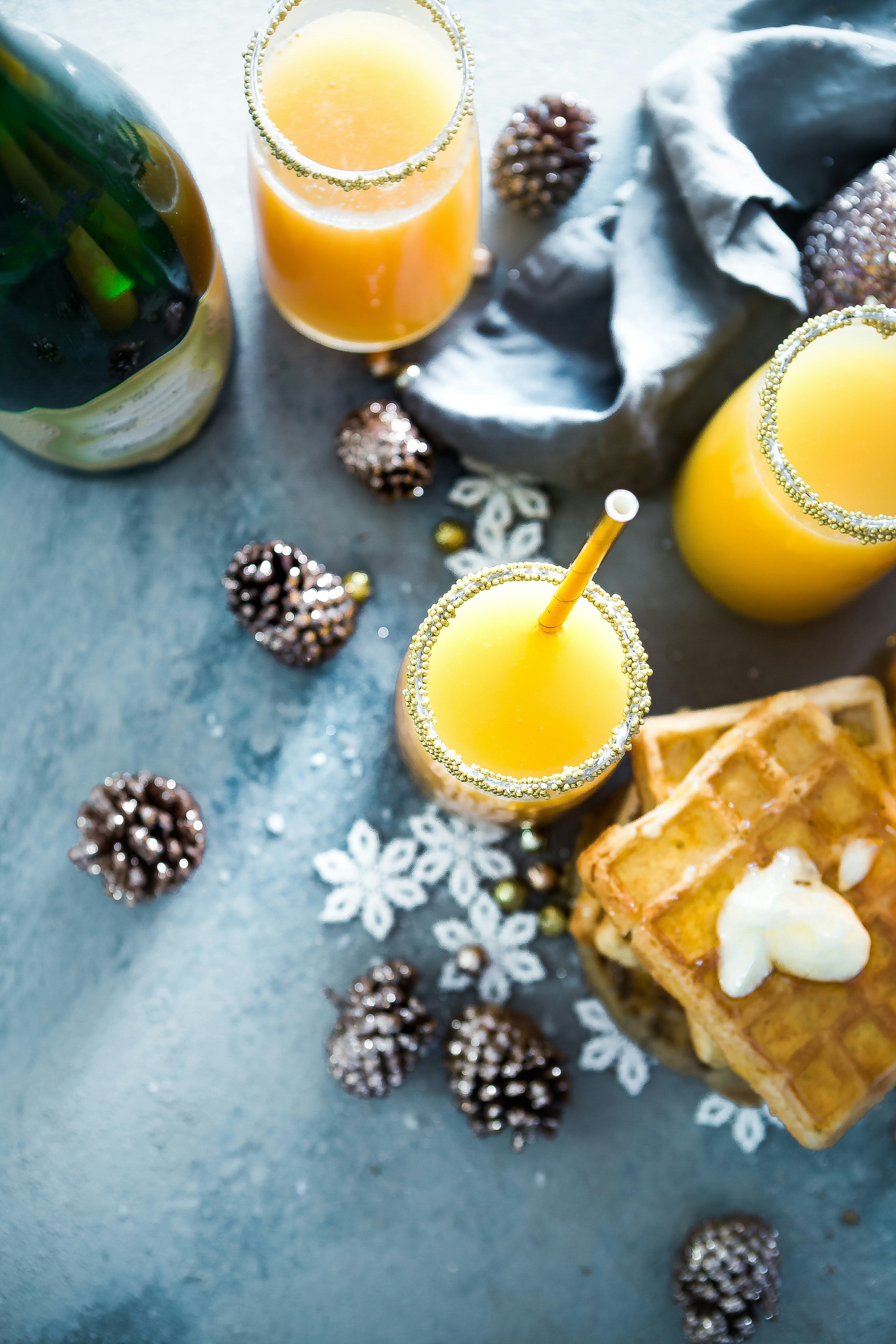 Three glasses of orange juice with waffles and pine cones and snowflakes around. - wallpaper image