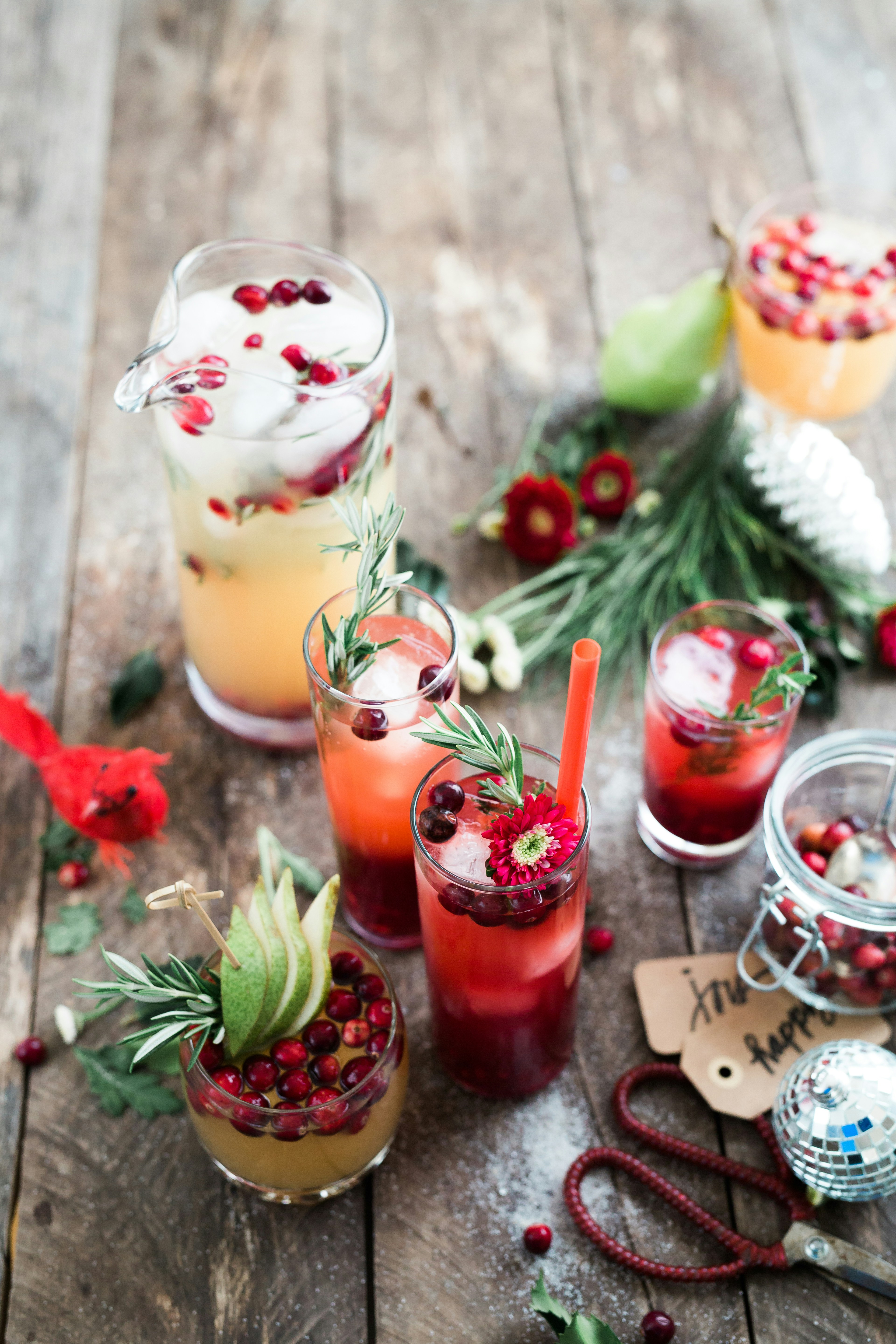 Several glasses of red wine are placed on a wooden table, decorated with red berries and green plants, with some Christmas decorations around them. - wallpaper image