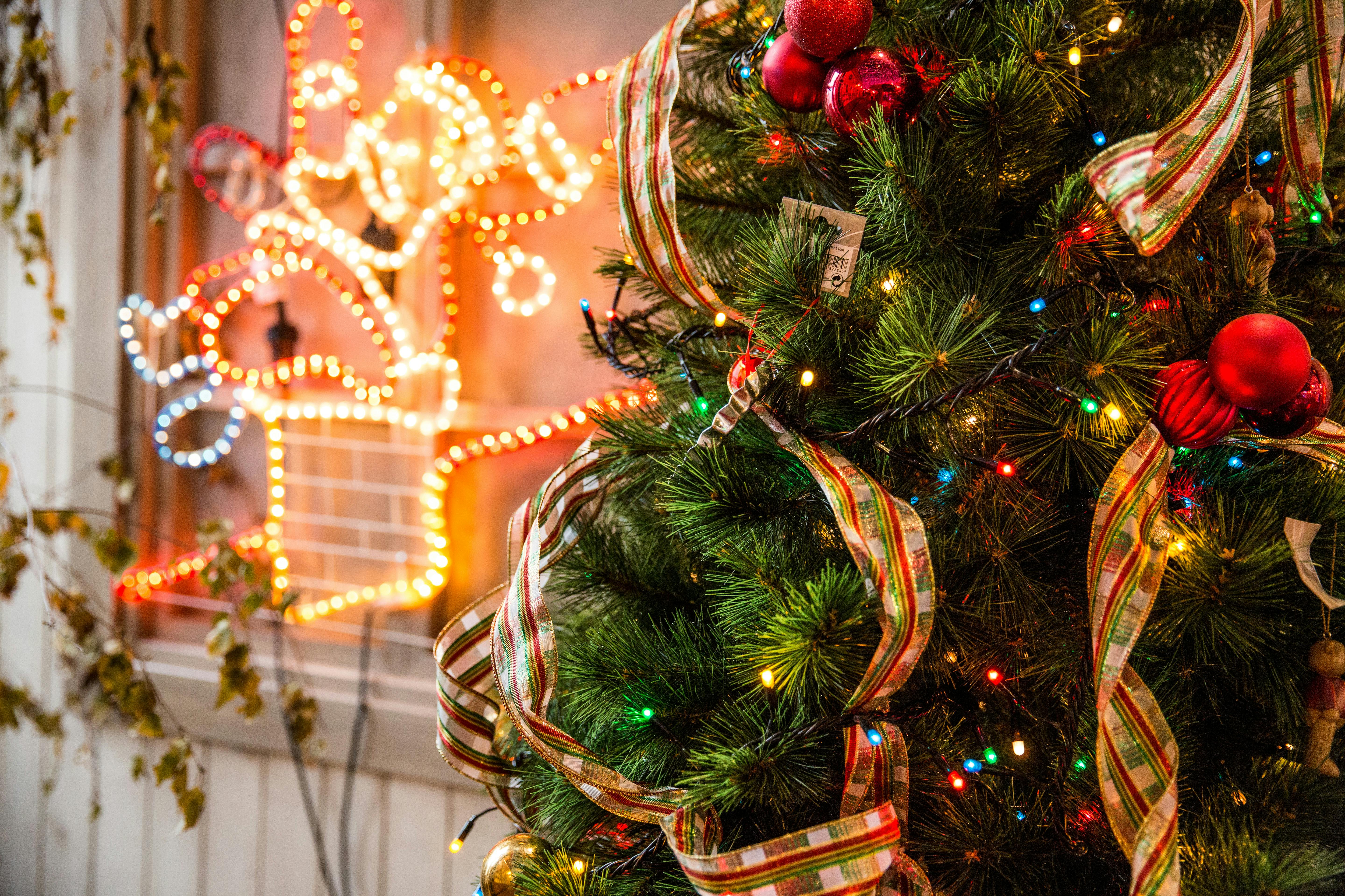 A Christmas tree is decorated with colorful lights, red balls, golden ribbons, and colorful baubles - wallpaper image