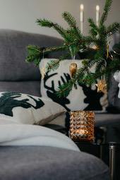 A Christmas tree decorated with gold ornaments is placed next to a sofa, with a glass cup with a lit candle beside it. - wallpaper image