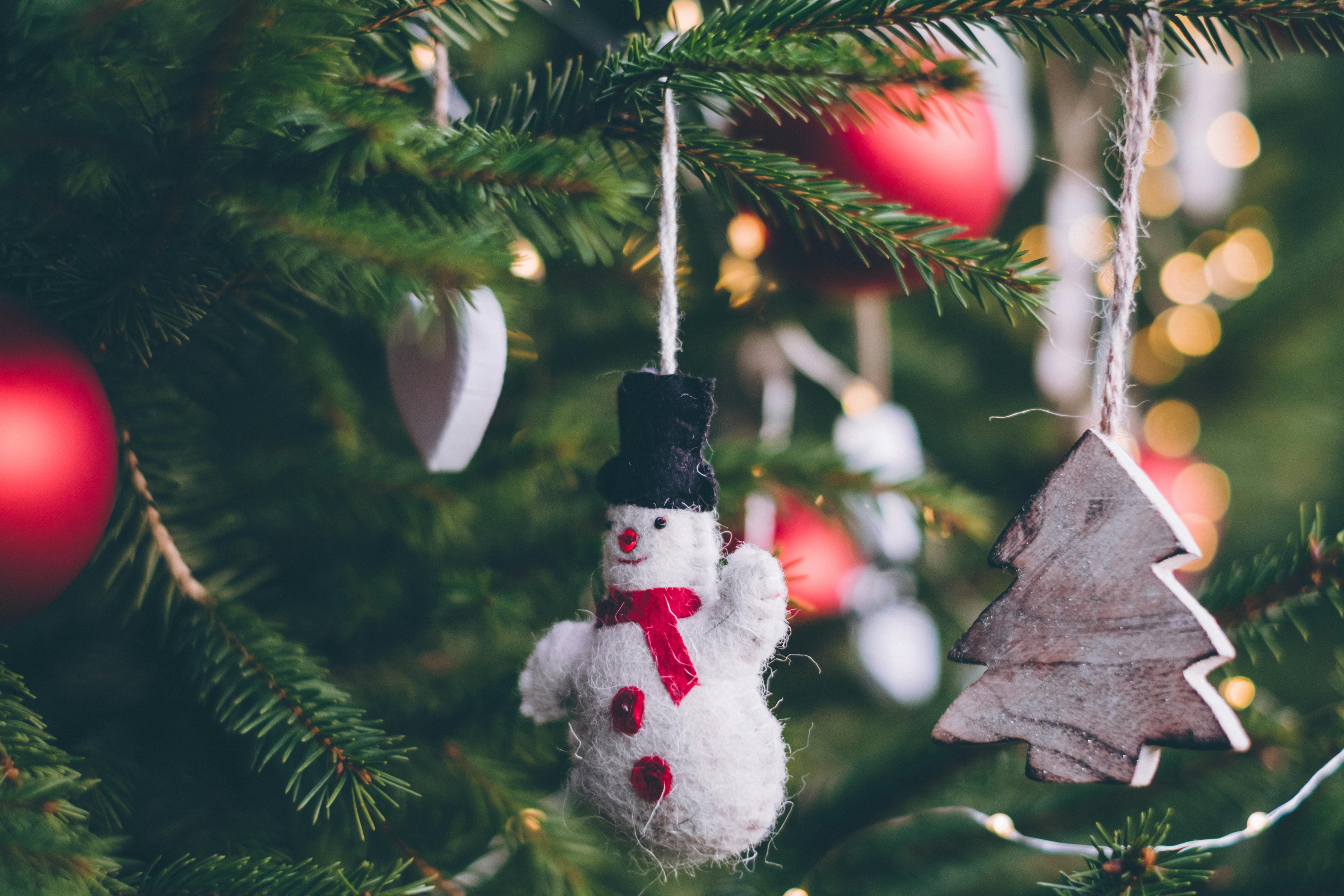 A Christmas tree is decorated with various ornaments, including a plush snowman, a wooden Christmas tree, and some red baubles. - wallpaper image