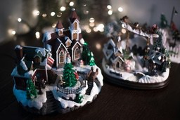 A model of a Christmas village with houses, a Christmas tree and figures, with a background of light decorations - wallpaper image