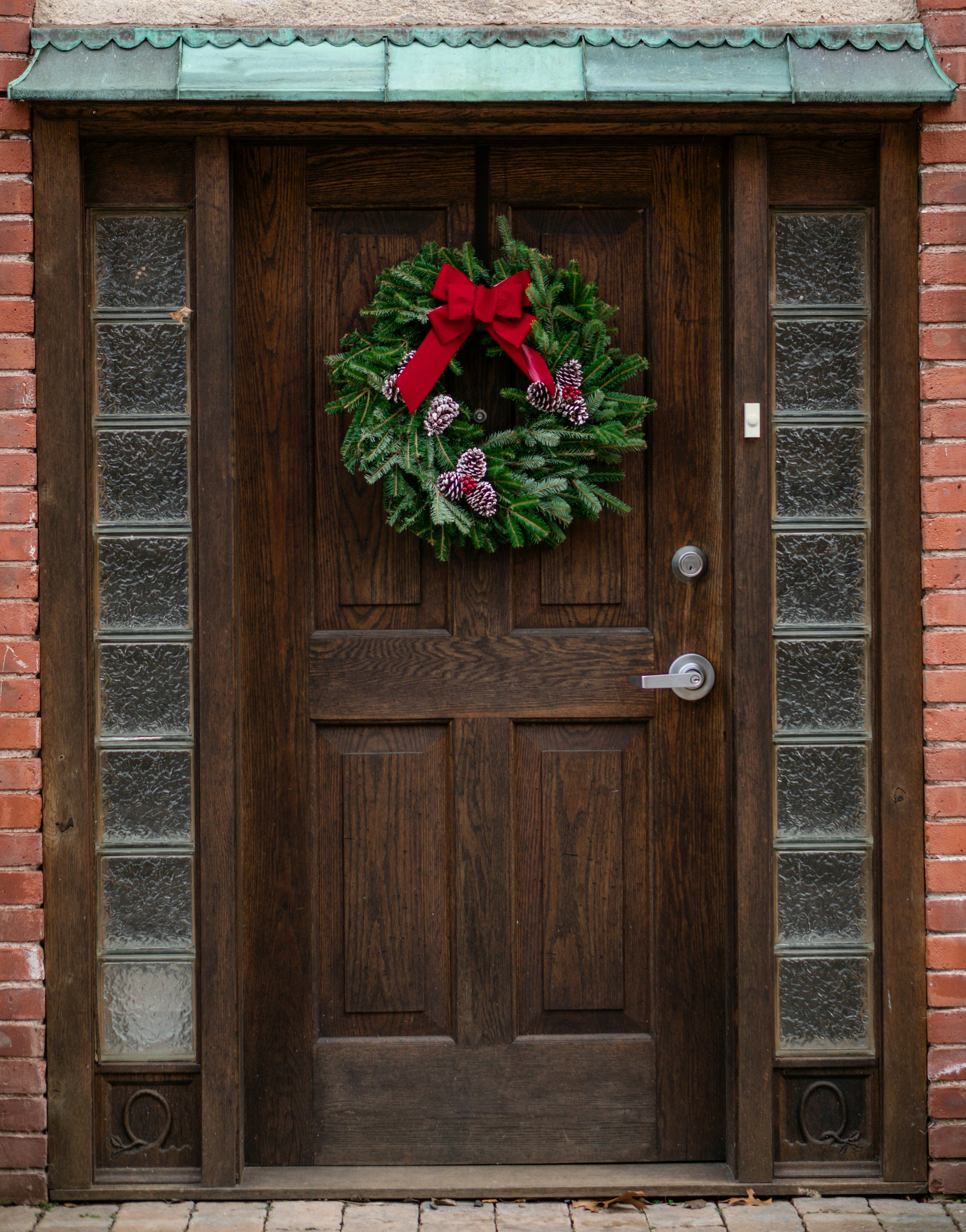 A wooden door is decorated with a Christmas wreath with a red ribbon and some pine cones. - wallpaper image