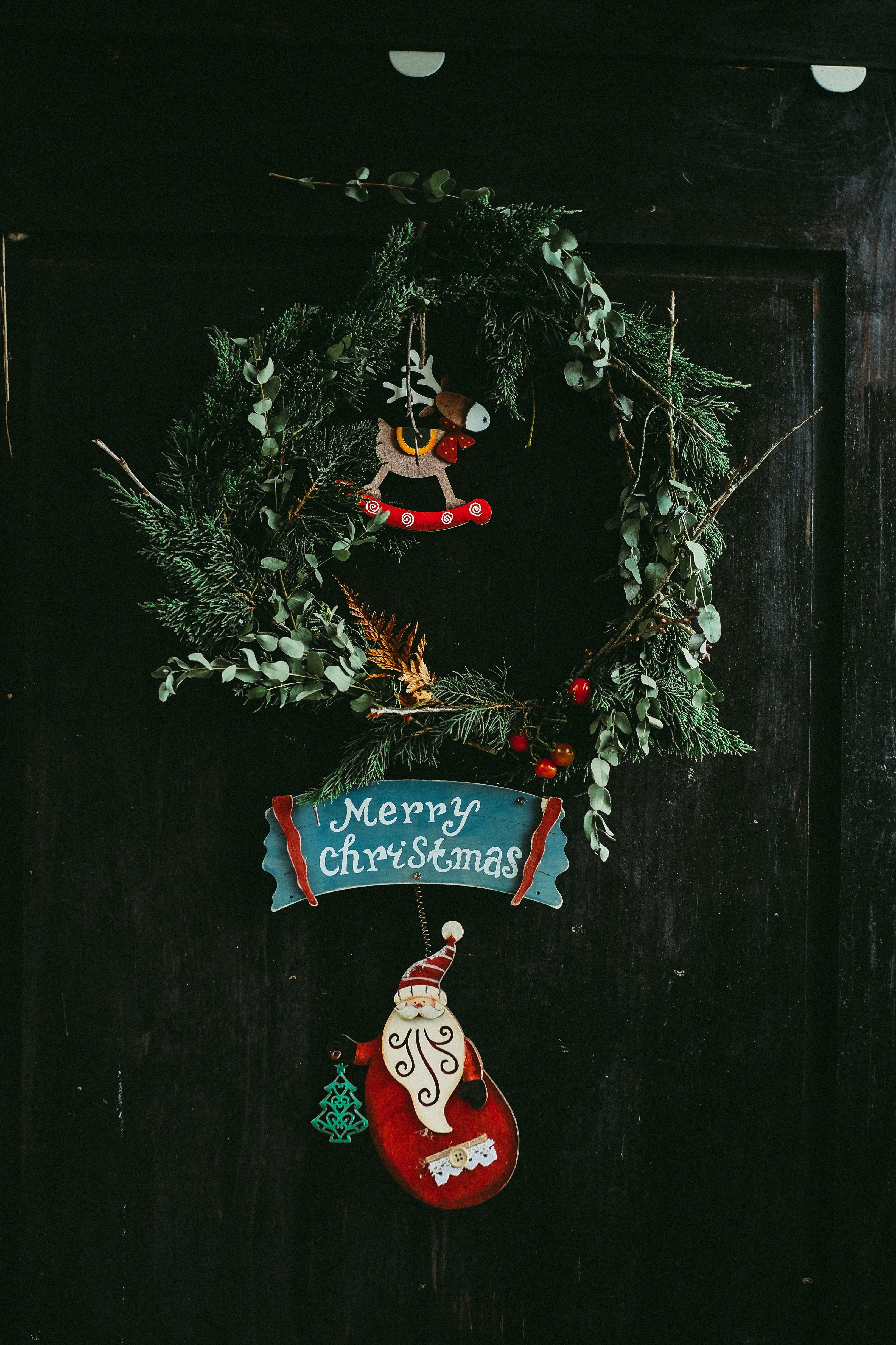 A wooden door with a Christmas wreath decorated with Santa Claus, reindeer and other Christmas elements, as well as the words "Merry Christmas". - wallpaper image