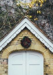 A white door decorated with a Christmas wreath, the brick wall above the door is covered with green vines. - wallpaper image