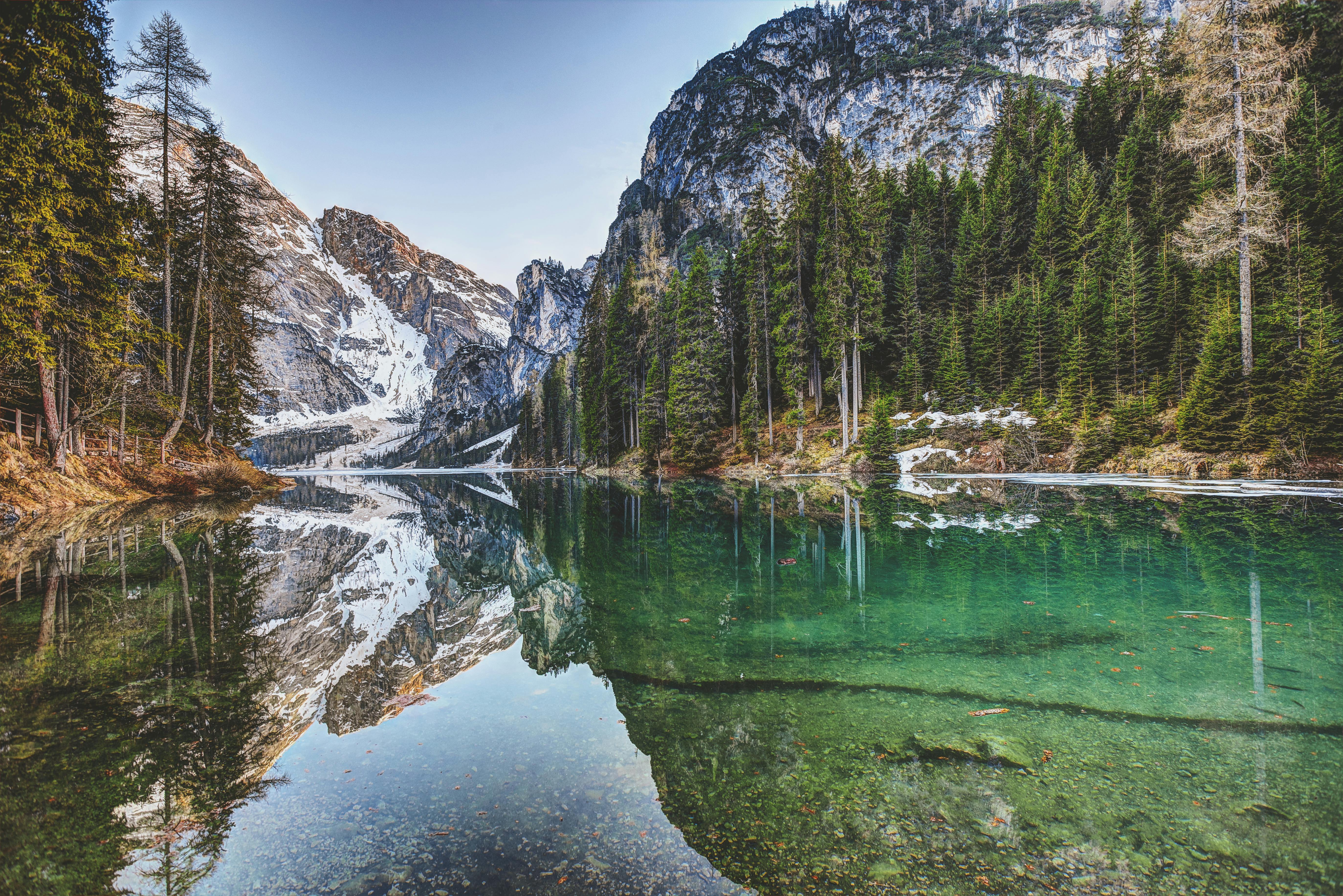 A mountain lake with clear water reflecting the snow-capped mountains and forests - free wallpaper image