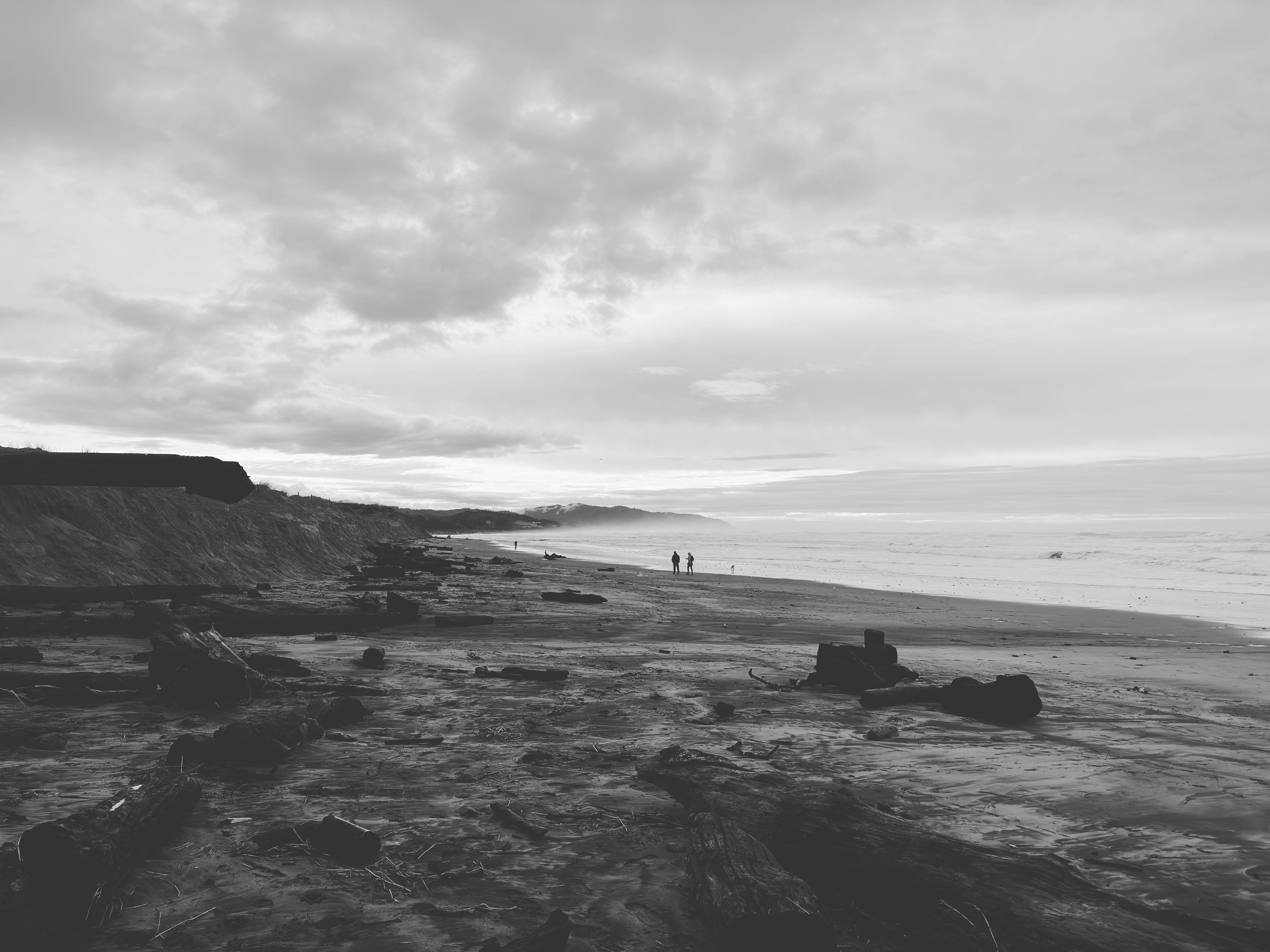 Several figures walk along the beach, with the sea in the distance and the sky full of clouds. - free wallpaper image