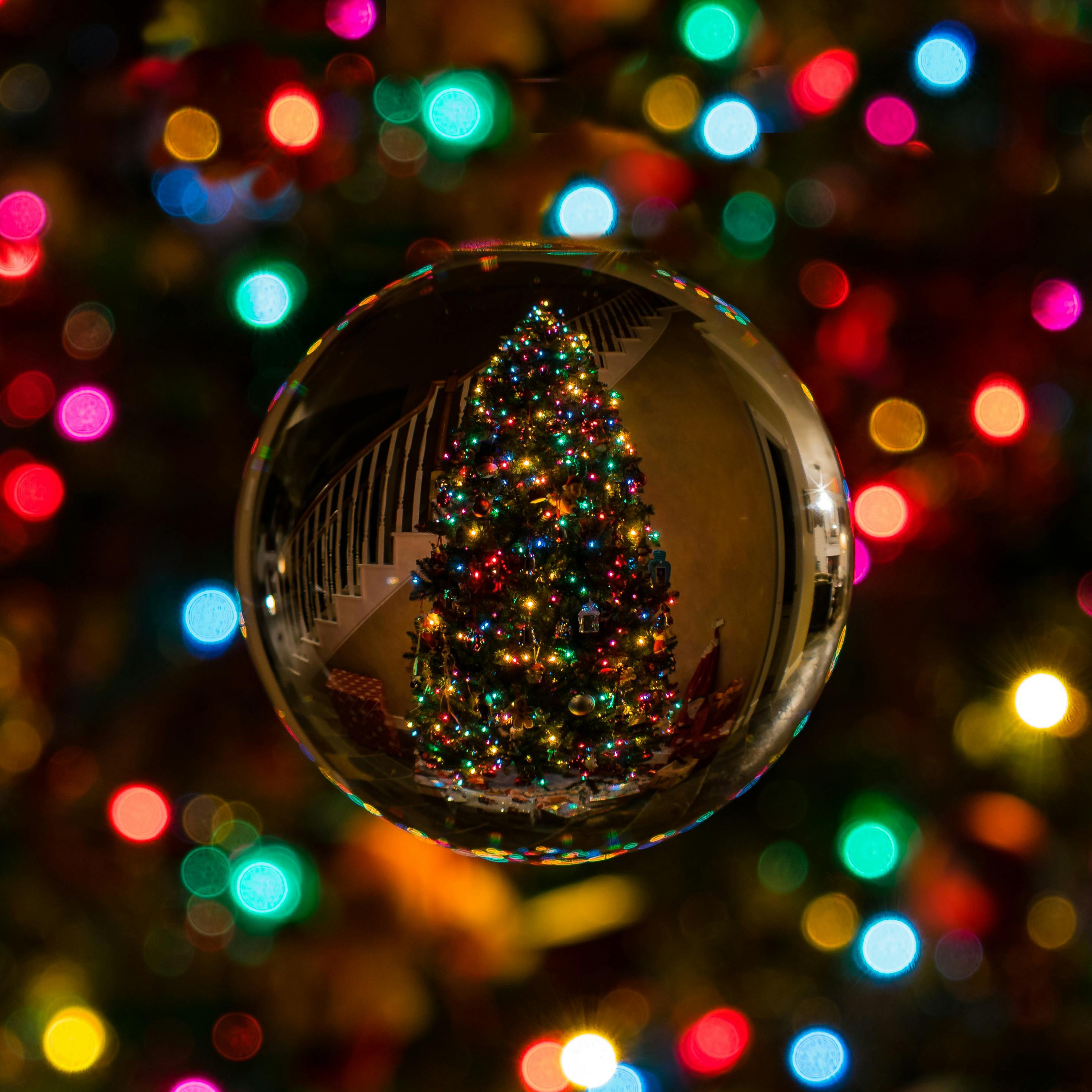 A crystal ball reflecting a Christmas tree decorated with colorful lights, with blurry lights surrounding it - wallpaper image