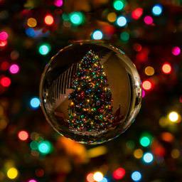 A crystal ball reflecting a Christmas tree decorated with colorful lights, with blurry lights surrounding it - wallpaper image