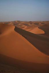 A group of tourists are walking on a sand dune in a vast desert, the sky in the distance is blue. - free wallpaper image