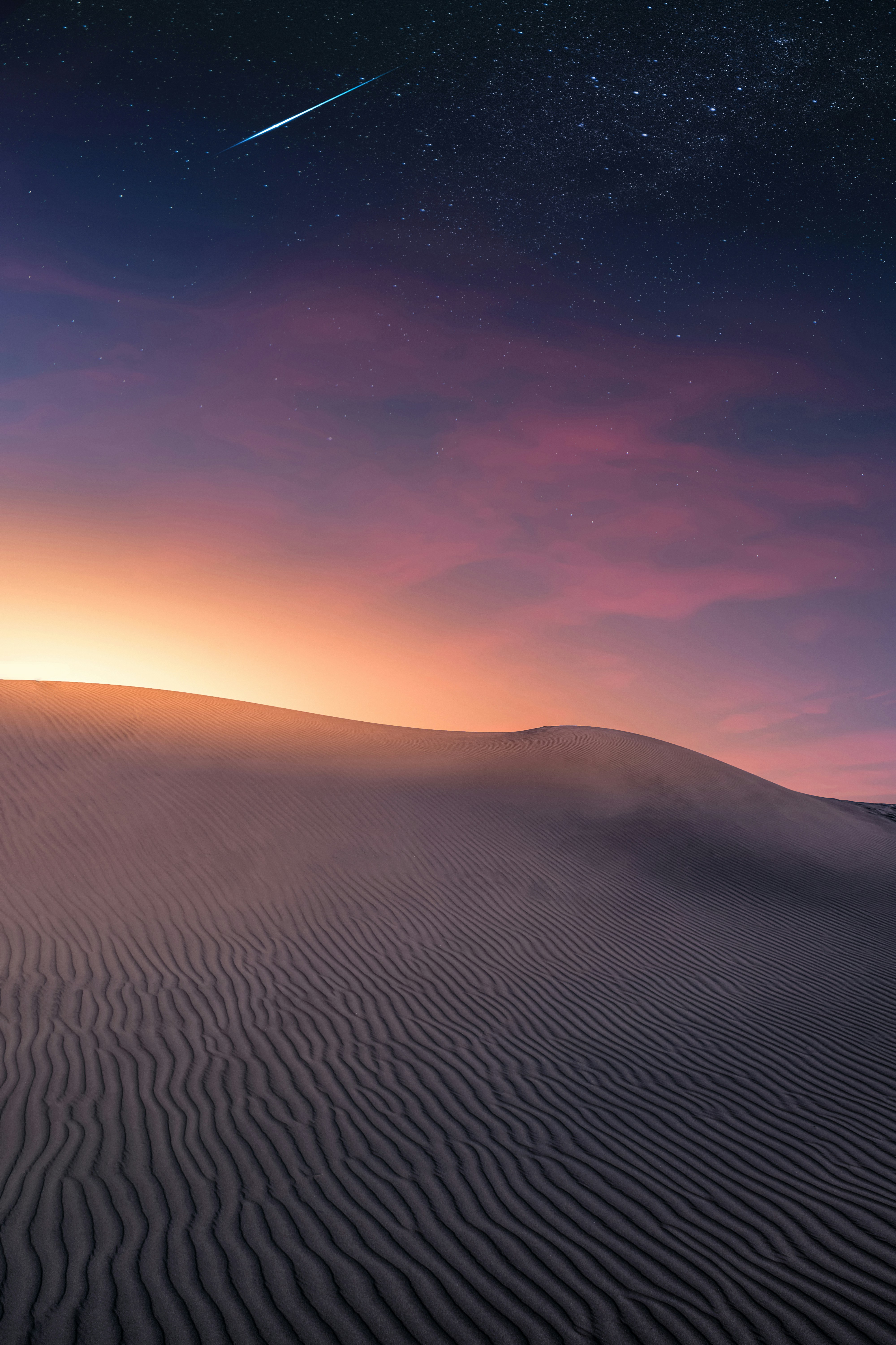 A shooting star appears in the sky over a white sand dune in the desert, against a background of purple, pink and orange night sky with stars. - free wallpaper image